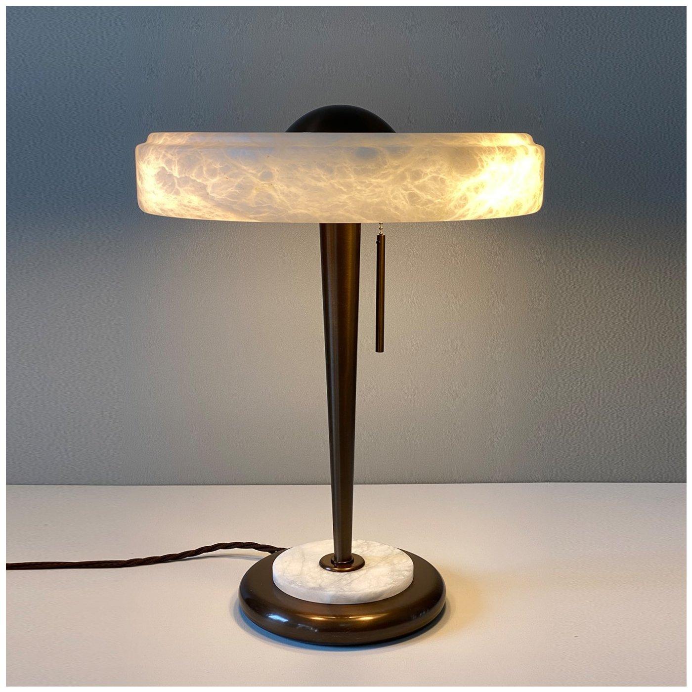 This stunning table lamp comes in a limited edition collection of 10 pieces. With its refined Art Deco flair, this elegant collector's item features an exquisitely handcrafted bronze and alabaster circular base, a sleek cone-shaped bronze body