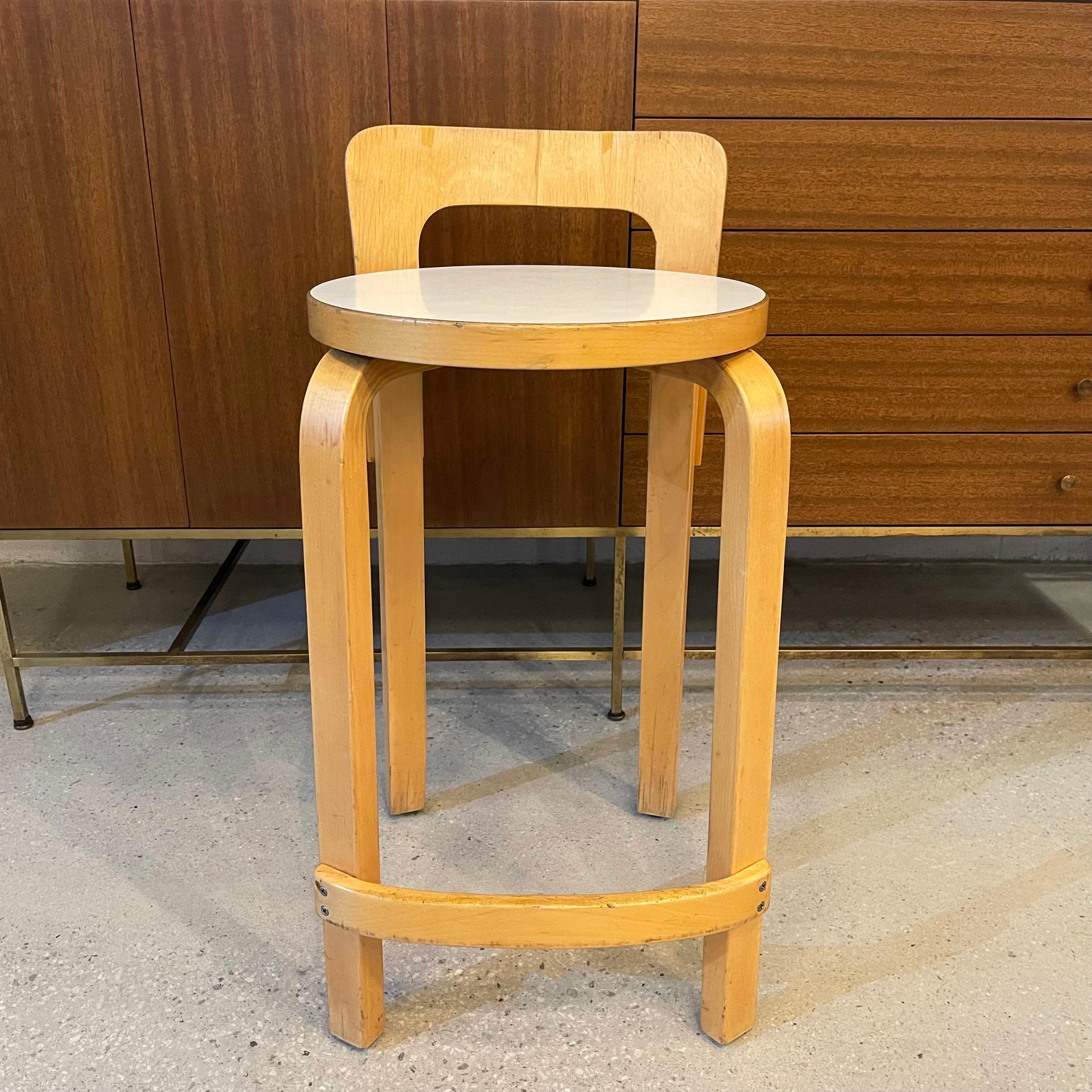 Mid-century modern, counter height stool designed by Alvar Aalto for Artek features a bent birch wood frame with white laminate 13 inch diameter seat. 