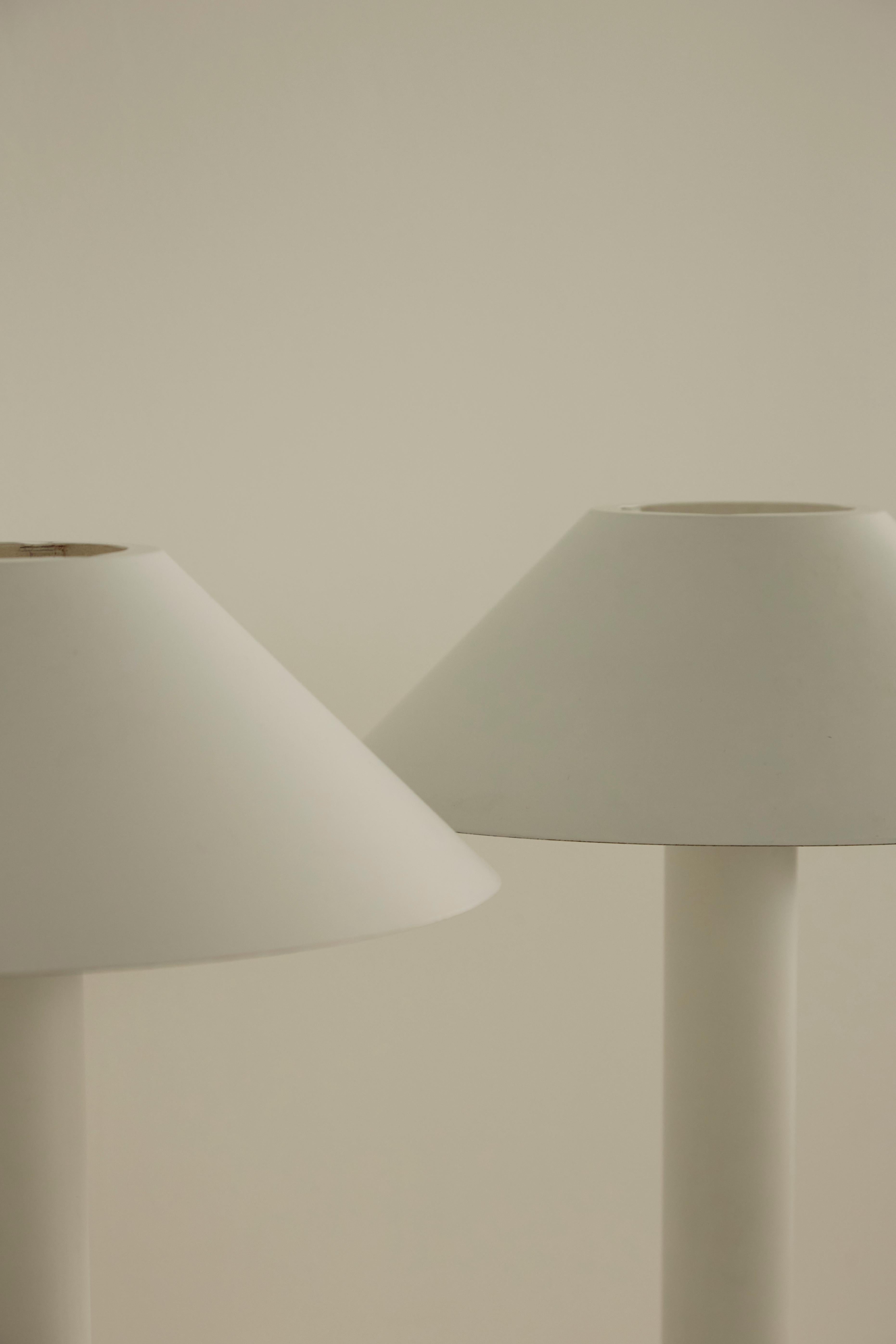 Paire de lampes de table blanches d'une élégante simplicité. Whiting : tiges cylindriques en métal laqué blanc, abat-jour coniques et bases profilées élégantes. Le prix correspond à la paire.