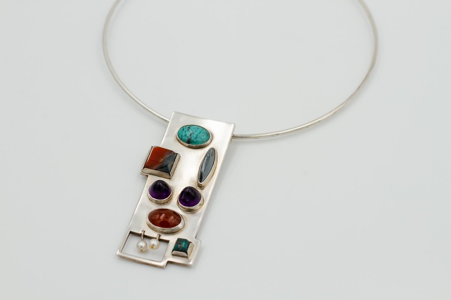 Very rare and unusual design.

Bent Knudsen; a rigid collar and modernist pendant
Sterling silver necklace, pendant set with cultured pearls, cabochon-cut turquoise, hematite, amethyst, carnelian and agate. 
Model #167
Rigid collar Diam 16 cm (6,3