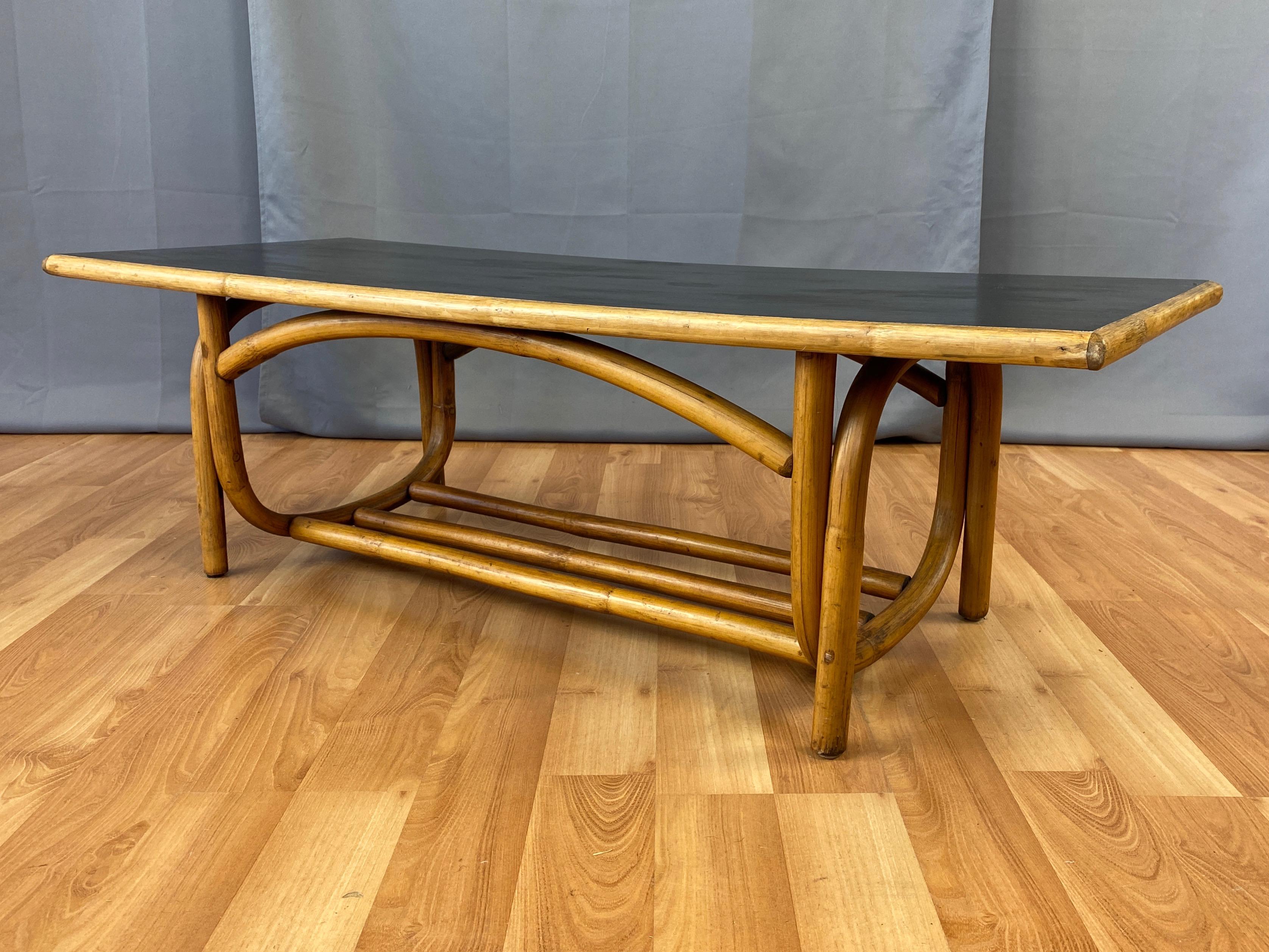 A very handsome 1950s bent rattan coffee table with black lacquered top, perfect for a boho chic interior or island vibe lanai.

Handcrafted of thick rattan with precisely executed curves and construction. Features a clever double U-shaped leg and