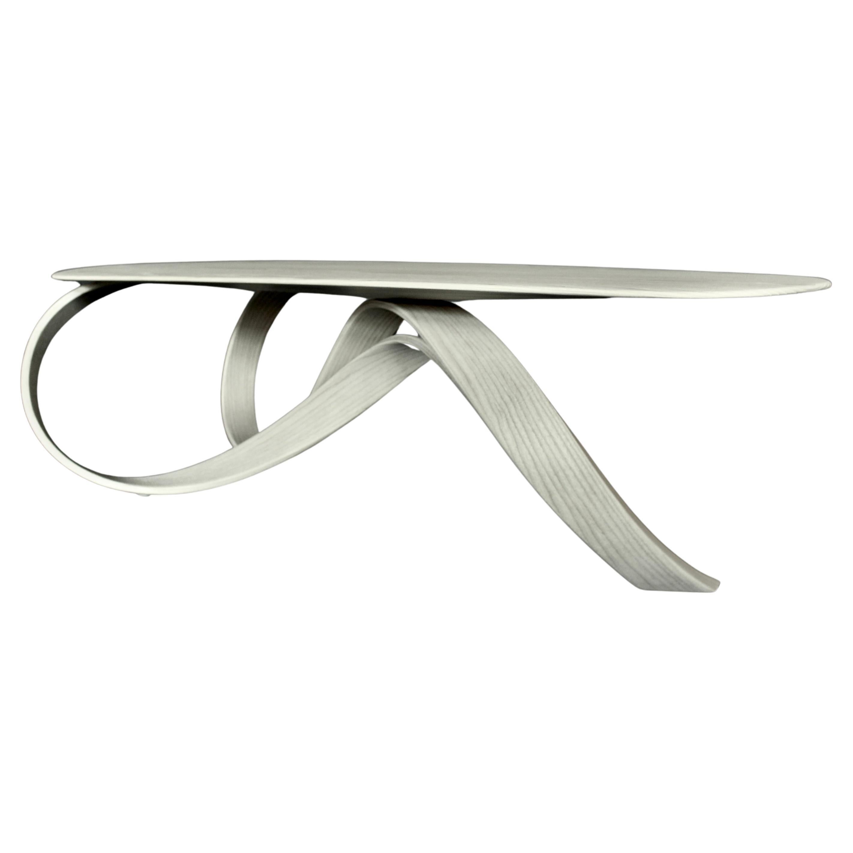 Cette table basse sculpturale témoigne de l'art du cintrage du bois, fabriquée en frêne massif et finie avec une huile teintée en blanc pour préserver sa beauté organique. La forme fluide de la table est obtenue grâce à une technique de laminage