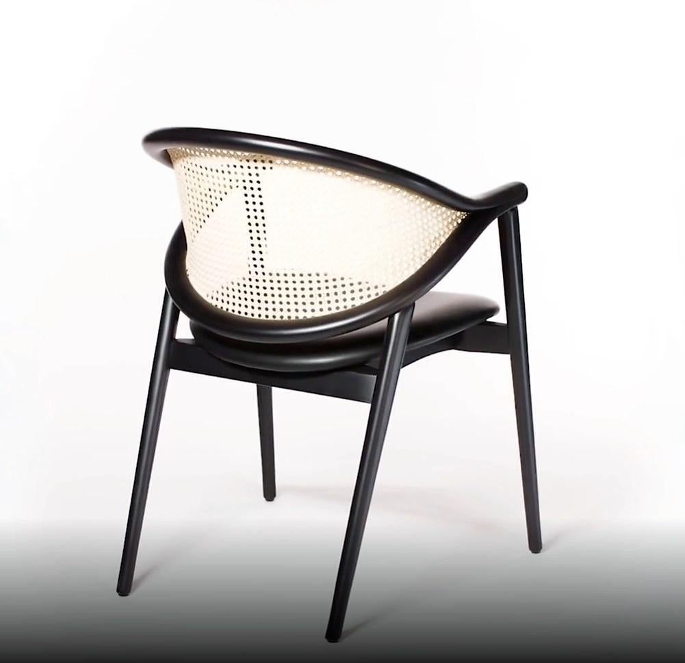 The chair is made of steam-bent wood and upholstered in Italian black leather. The manufacturing of the item requires a manual installation of the cane that needs artisanal craft and creates an elaborate interplay with the bentwood