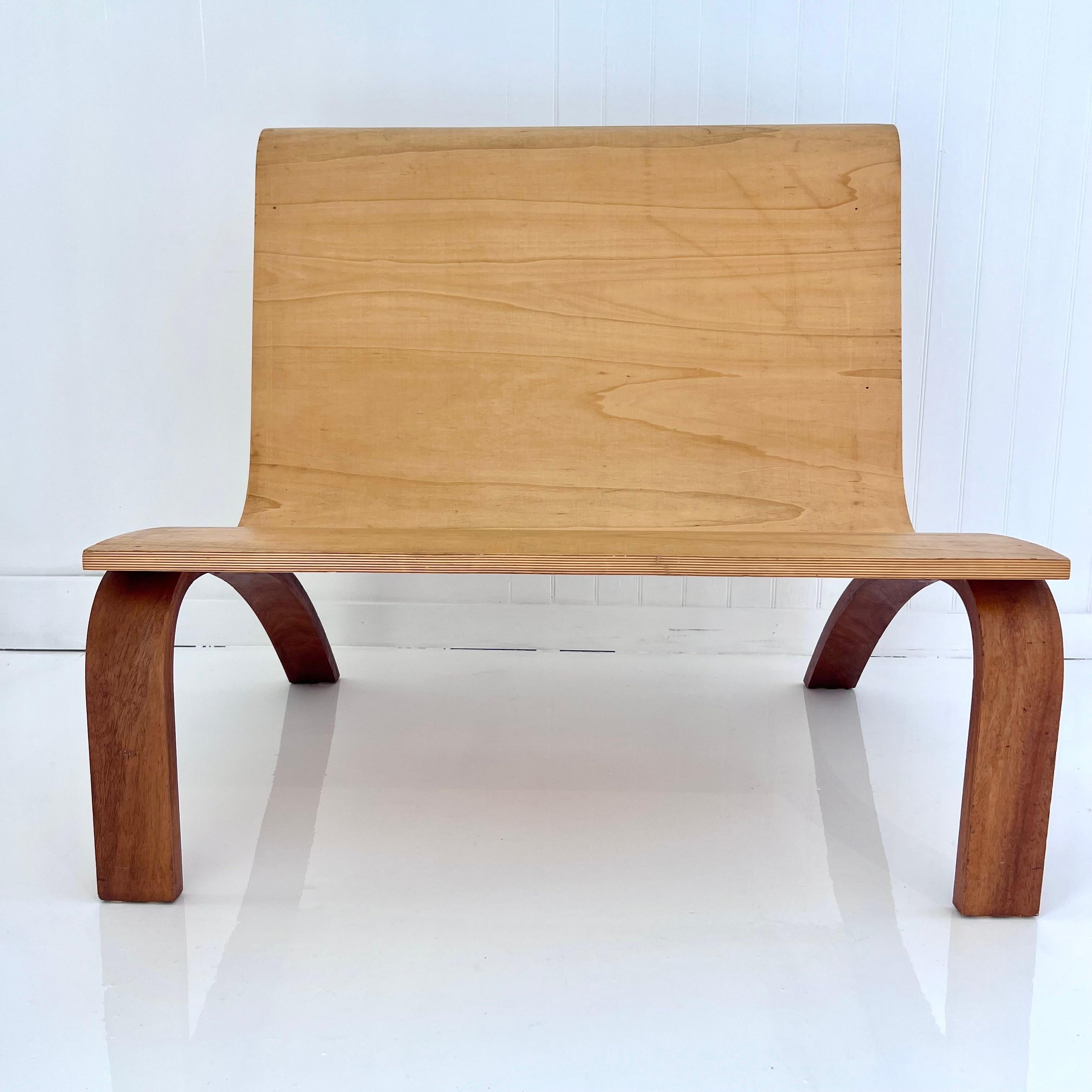 Minimalistische Bugholzbank mit Rückenlehne und Sitzfläche aus Sperrholz und kontrastierenden Beinen aus dunklem Holz. Die schöne Wölbung bietet einen bequemen Sitz für einen oder zwei Erwachsene. Diese Bank zeichnet sich durch eine atemberaubende