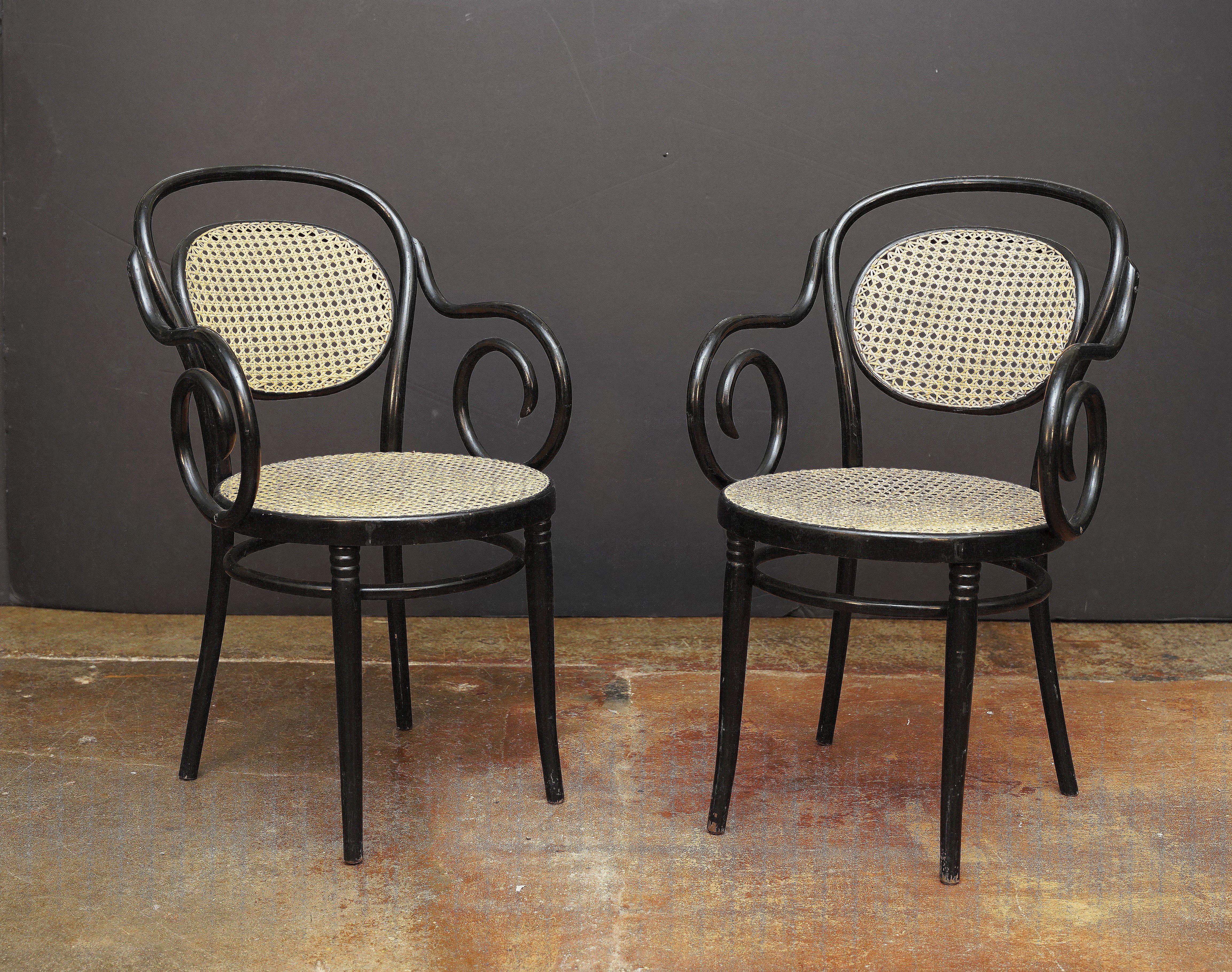 Fauteuil italien en bois courbé avec une élégante structure peinte en noir - comprenant un dossier en forme avec un dossier canné et des accoudoirs en volute avec une assise cannée reposant sur quatre pieds avec une base à brancard rond.

Deux