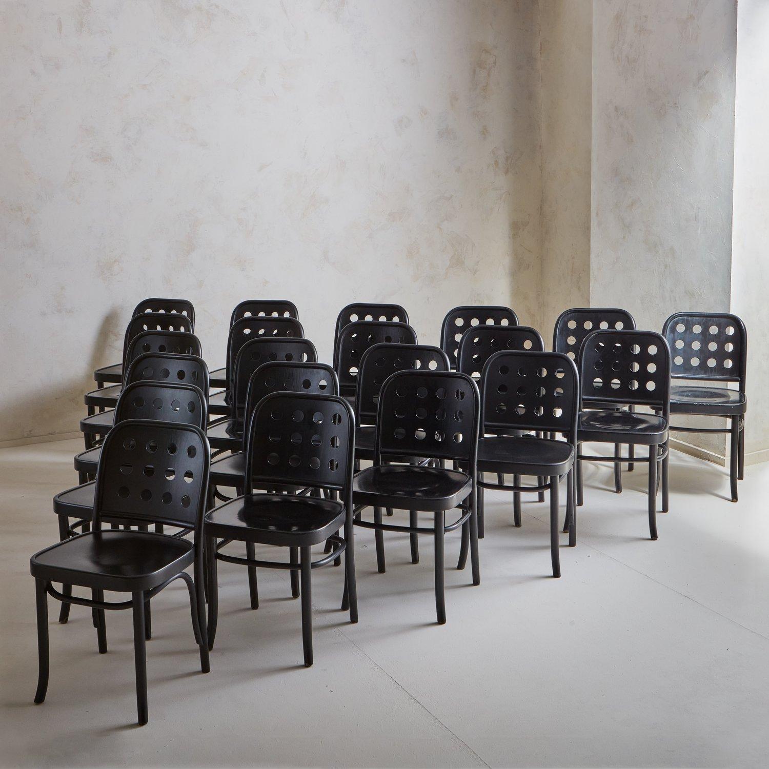 A set of 11 dining chairs designed by Josef Hoffmann + Oswald Haerdtl circa 1928 and produced by Thonet. These chairs were constructed with bent plywood and painted black. They have sleek silhouettes and feature nine circular cutout details on the