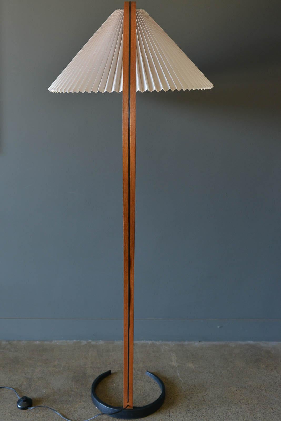 Mads Caprani floor lamp, circa 1971 by Danish manufacturer Mads Caprani AS. This vintage lamp features sculptural bent plywood stand with en elegant curve, a cast iron crescent shaped base, and original pleated linen shade. Original floor switch and