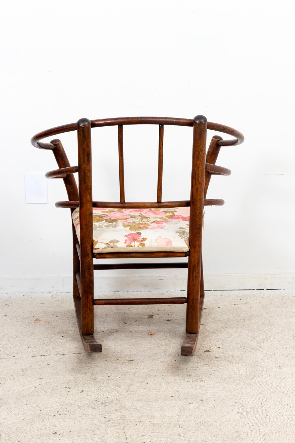 Circa early 20th century vintage bentwood rocking chair with curved seat back, floral seat cushion, and box stretcher on the base. The piece was most likely manufactured by the Hickory Chair Company. Made in the United States. Please note of wear