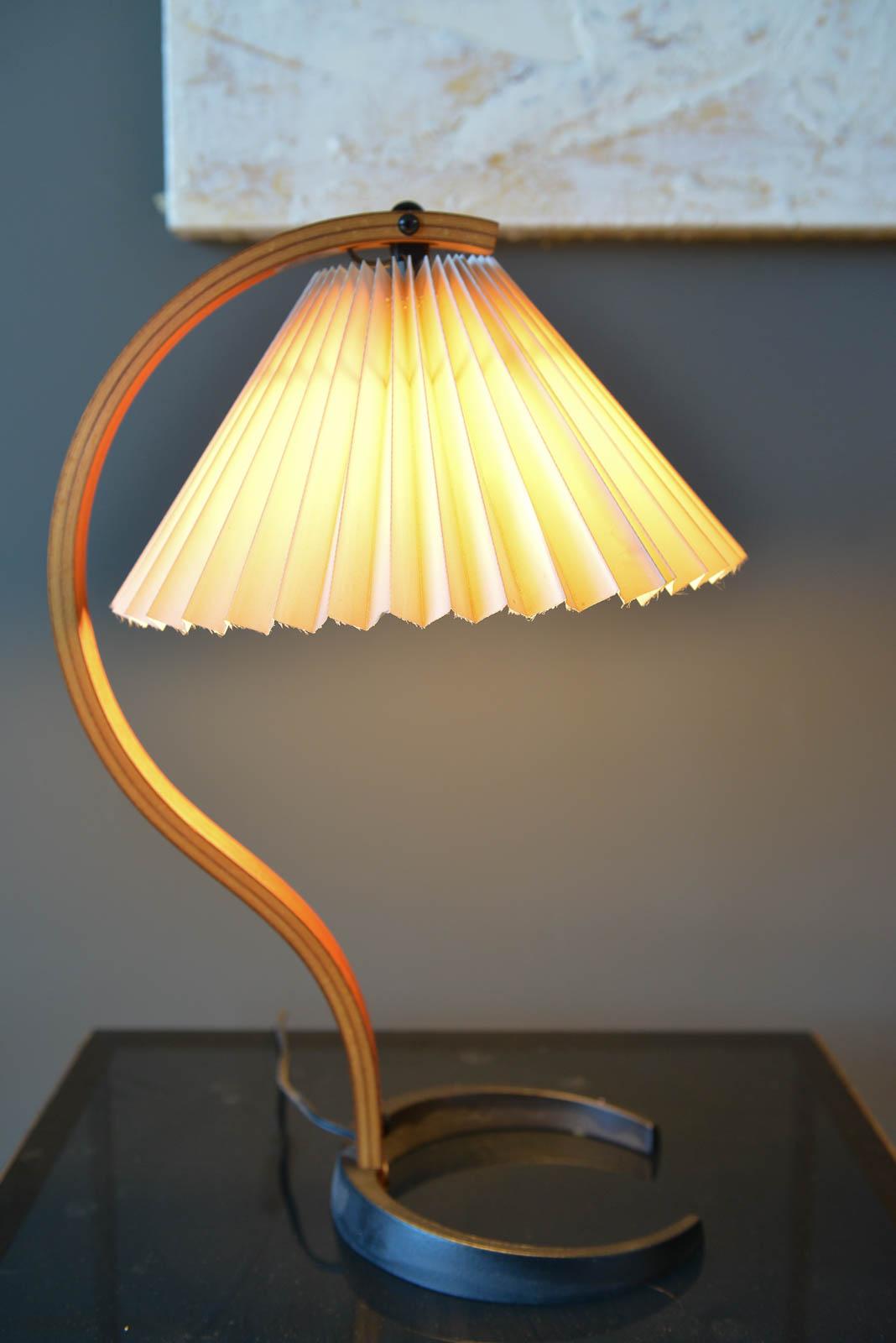 Mads Caprani table lamp, circa 1971 by Danish manufacturer Caprani Light AS. This vintage lamp features sculptural bent plywood stand with en elegant curve, a cast iron crescent shaped base, and original pleated linen shade. Original switch and