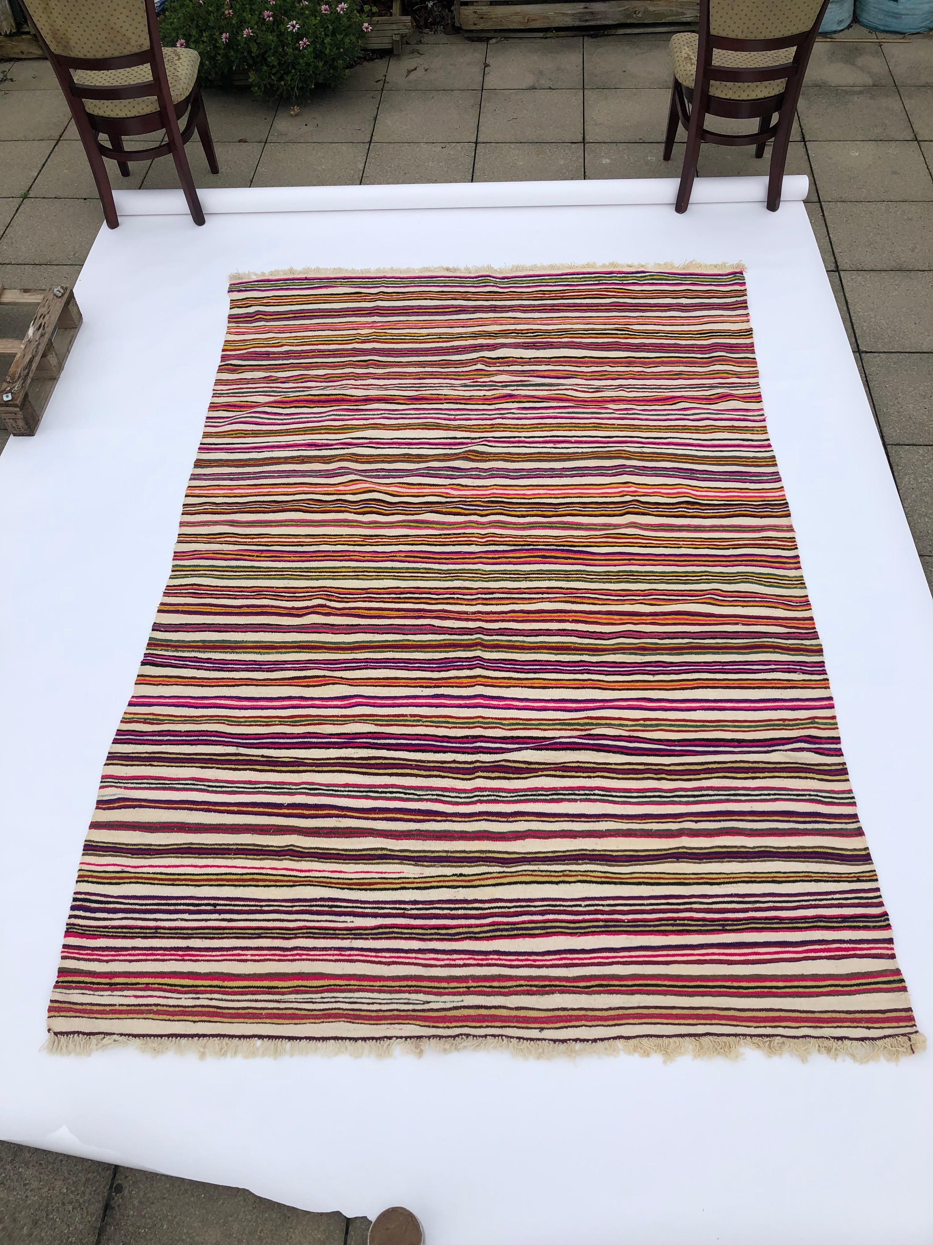 A large vintage Berber Algerian rug with colorful bold stripes dominated by pink fuchsia, yellow, and brown on beige background is a stunning handwoven piece.

This rug is handwoven using traditional techniques by Berber tribes in Algeria, and the