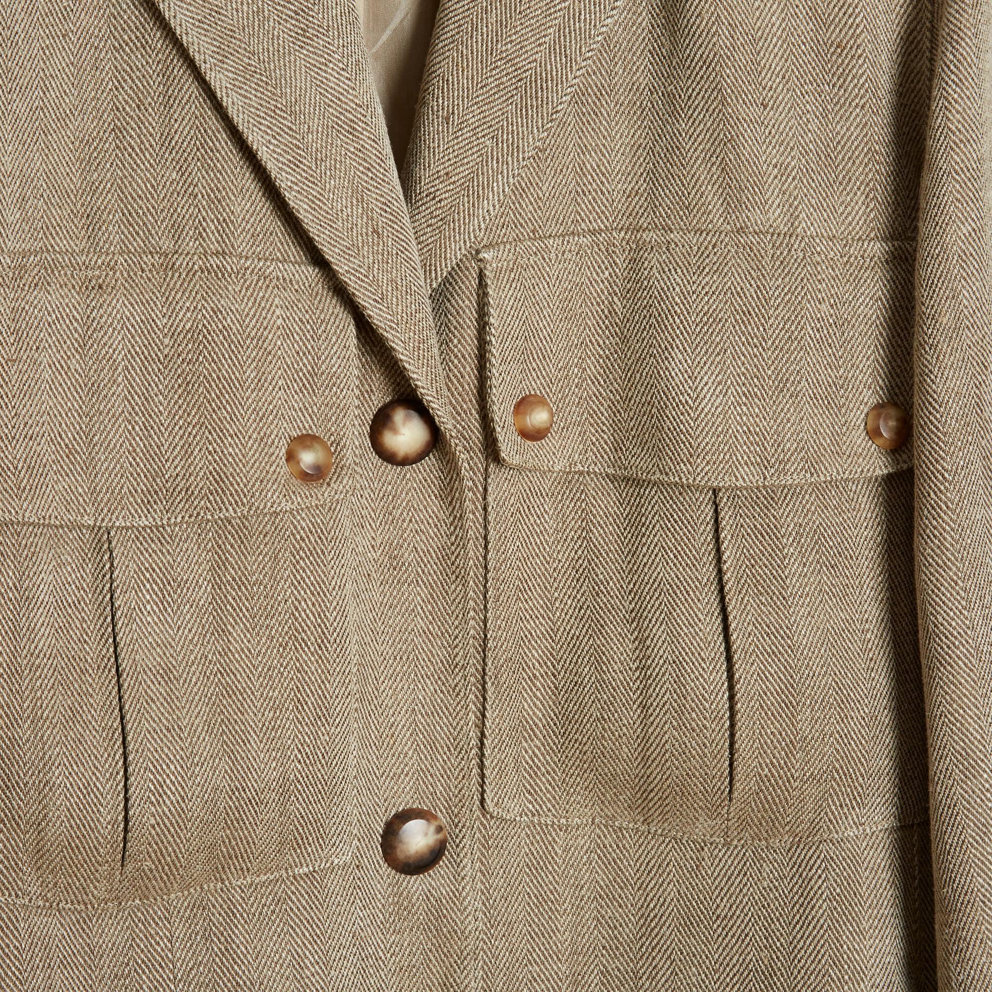 Manteau Anne-Marie Beretta en lin (et probablement en laine) à chevrons beiges, coupe presque droite, petit col cranté fermé devant par 3 boutons, 2 poches boutonnées à rabat sur la poitrine, 2 poches fermées par un zip invisible sur les côtés,