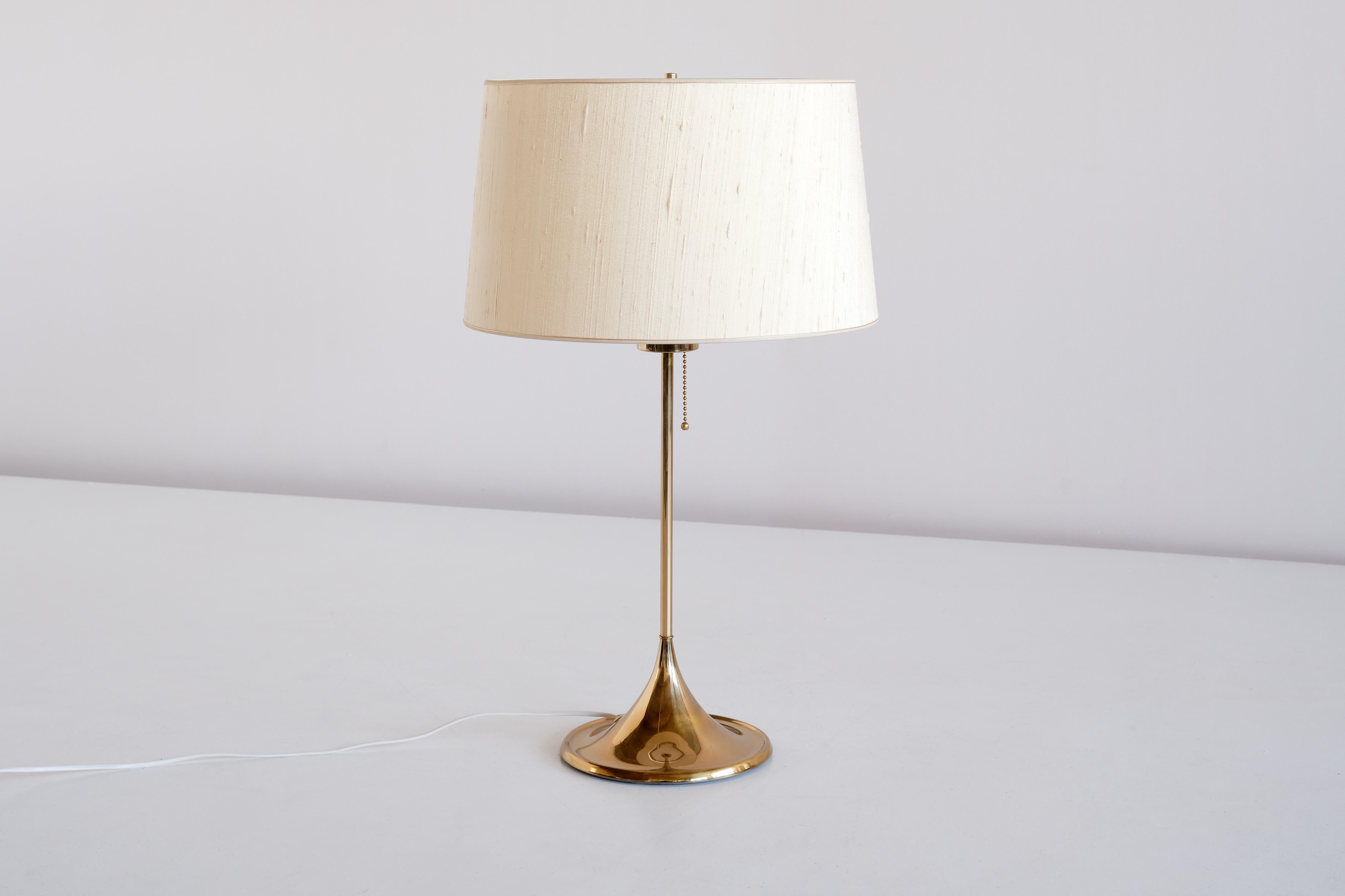 This elegant table lamp was produced by Bergboms in Sweden in the 1960s. The model is numbered B-024.
The lamp consists of a polished brass stem and cone shaped base, acrylic top diffuser and a newly handmade shade. The texture of the beige silk