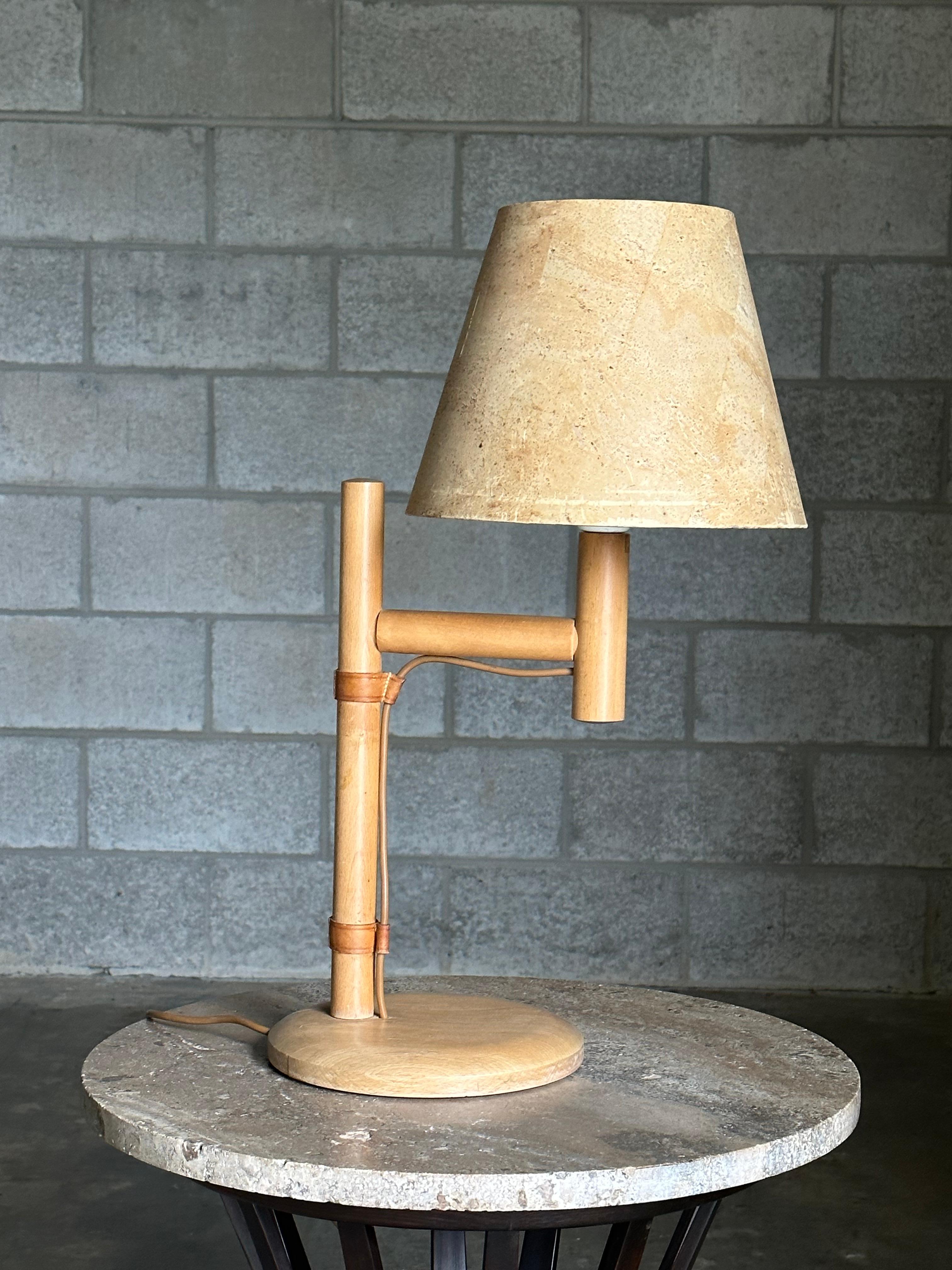 Une lampe de table inhabituelle produite en Suède par Bergboms vers les années 1960. La lampe se compose d'un corps en bouleau ou en hêtre, d'un cordon apparent, de lanières de cuir et d'un abat-jour en liège. La lampe pourrait être utilisée dans de