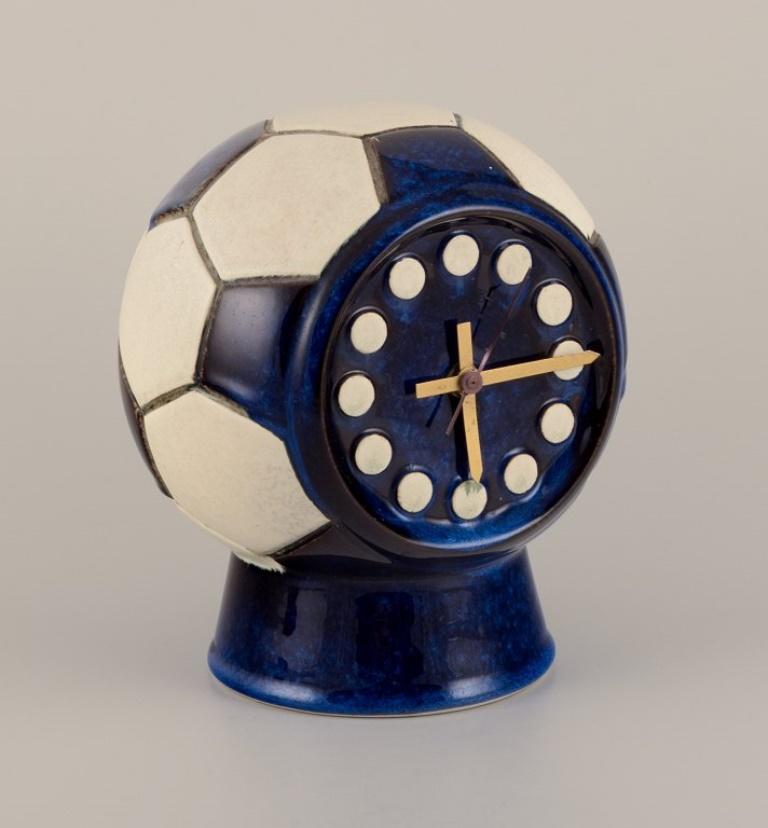 Berit Sundell for Gustavsberg, Sweden. 
Unique ceramic tabletop clock designed in the shape of a soccer ball. 
Brass hands.
Quartz movement.
Approximately 1970.
Signed.
Dimensions: Width 17.0 cm x Height 21.5 cm.
