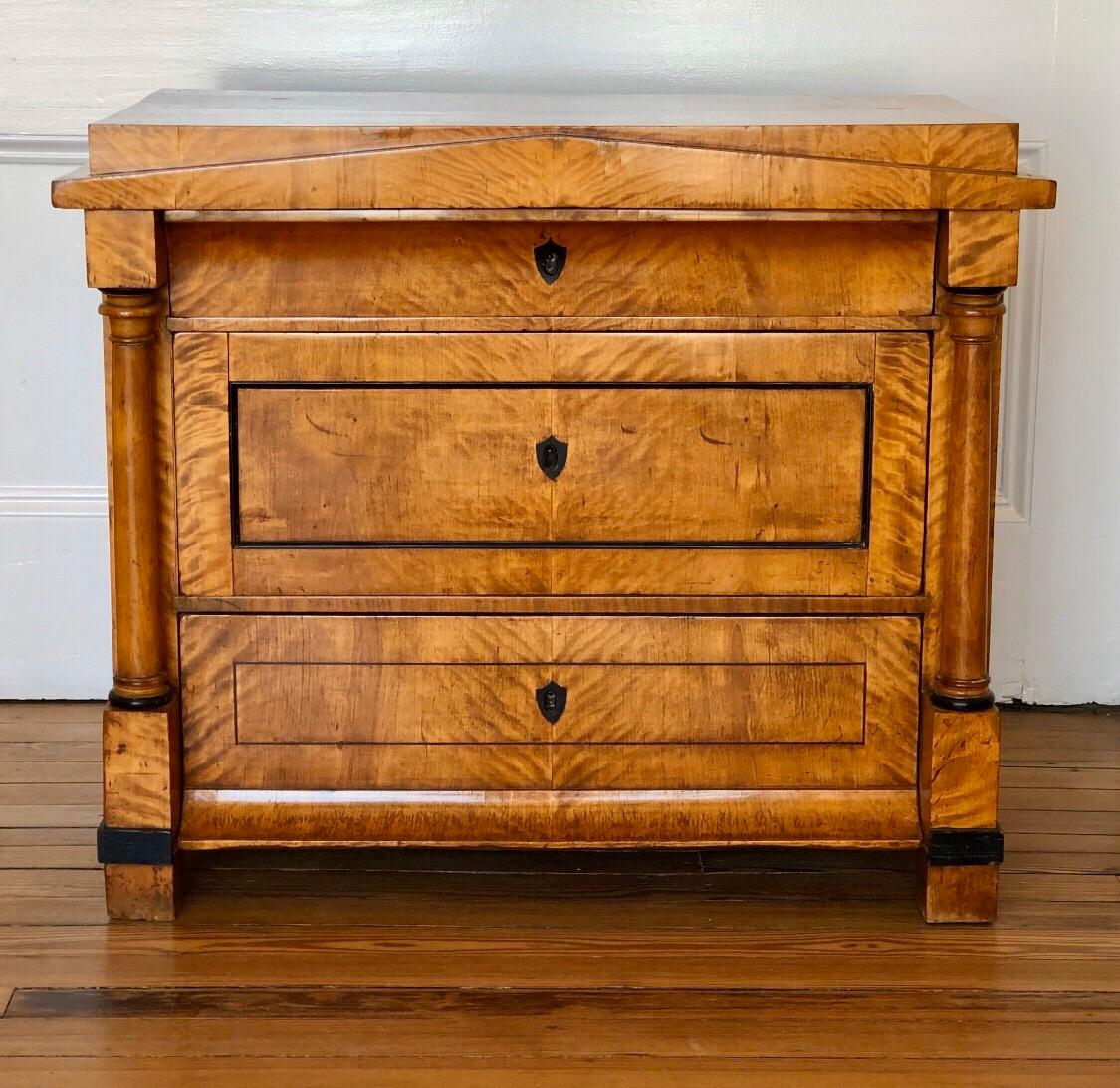 This 19th Century German Biedermeier chest with its classical architecture of doric pediments, and columns has a regal sophistication. The classic proportions and birch root veneer with ebony inlaid highlights of this chest of drawers creates a