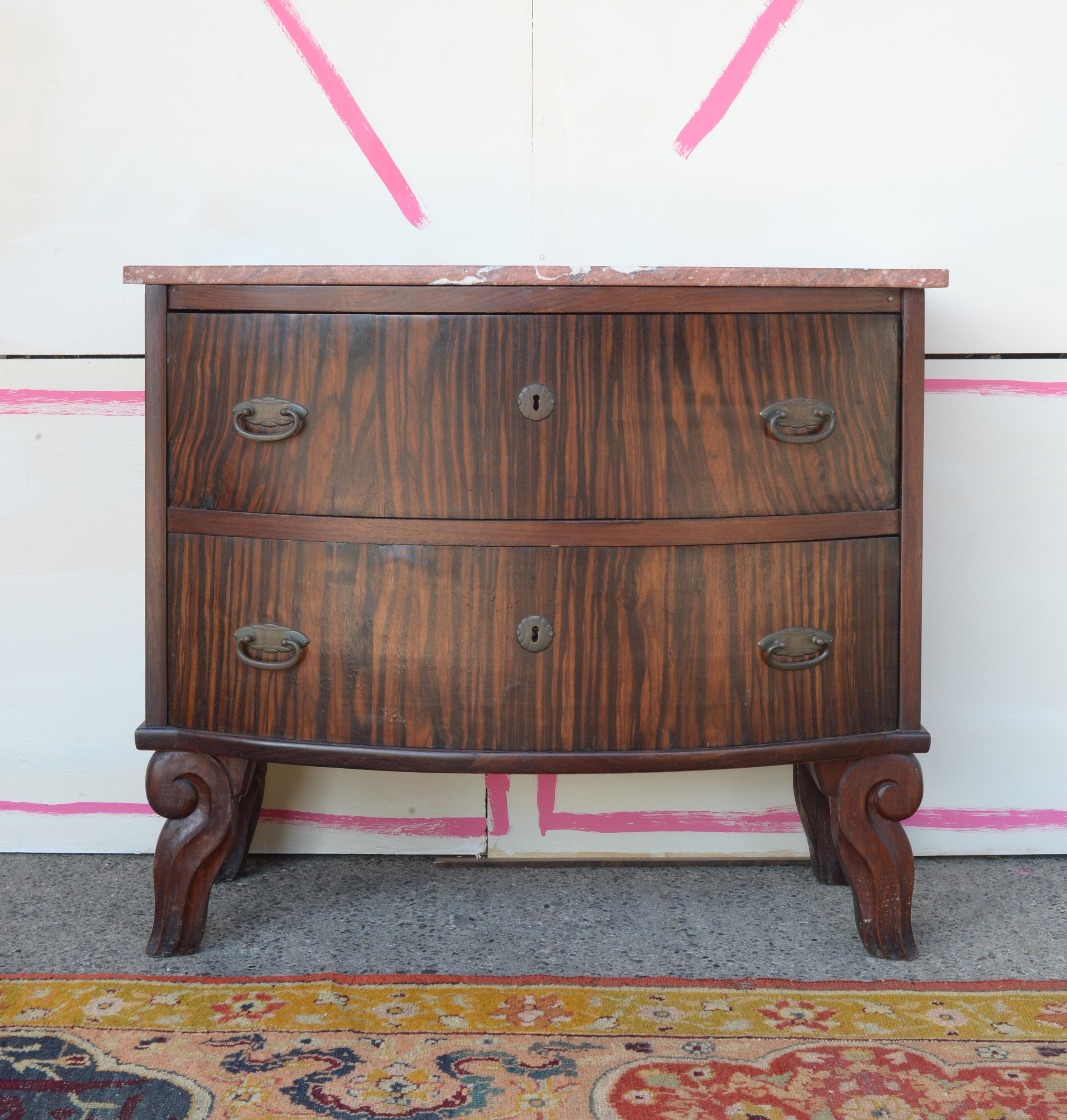 Esta cómoda de dos cajones es un buen ejemplo de mueble de principios del siglo XX de Alemania del Norte, de alrededor de 1910. La pieza presenta un frente suavemente bombeado (convexo) y una chapa de madera bellamente labrada -sobre todo en los