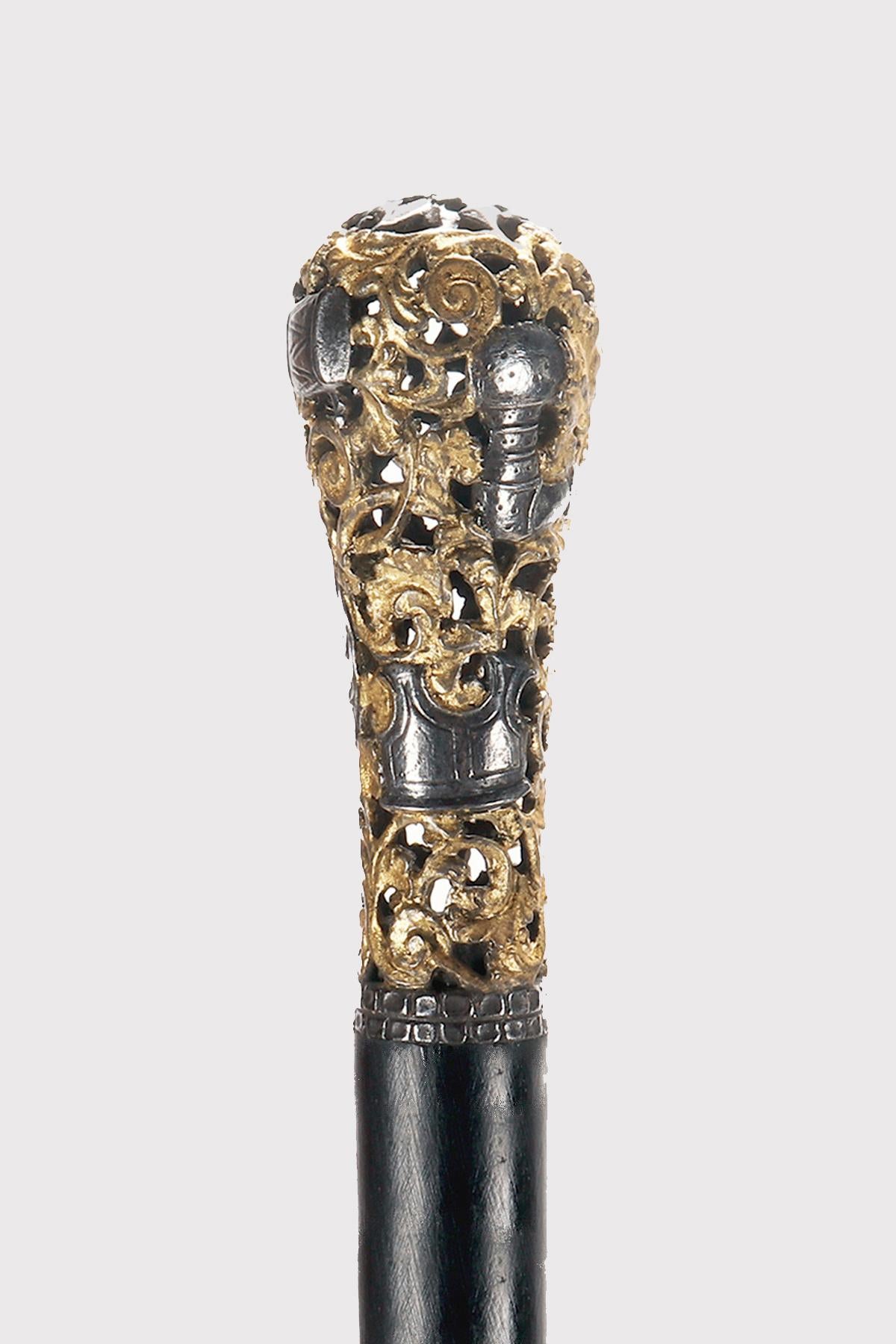Bastón: joya Bastón, pomo milord de hierro berlinés perforado, con grabados en relieve y dorados, que representan partes de armaduras. Vástago de madera de ébano. Virola metálica.  Alemania, hacia 1800.