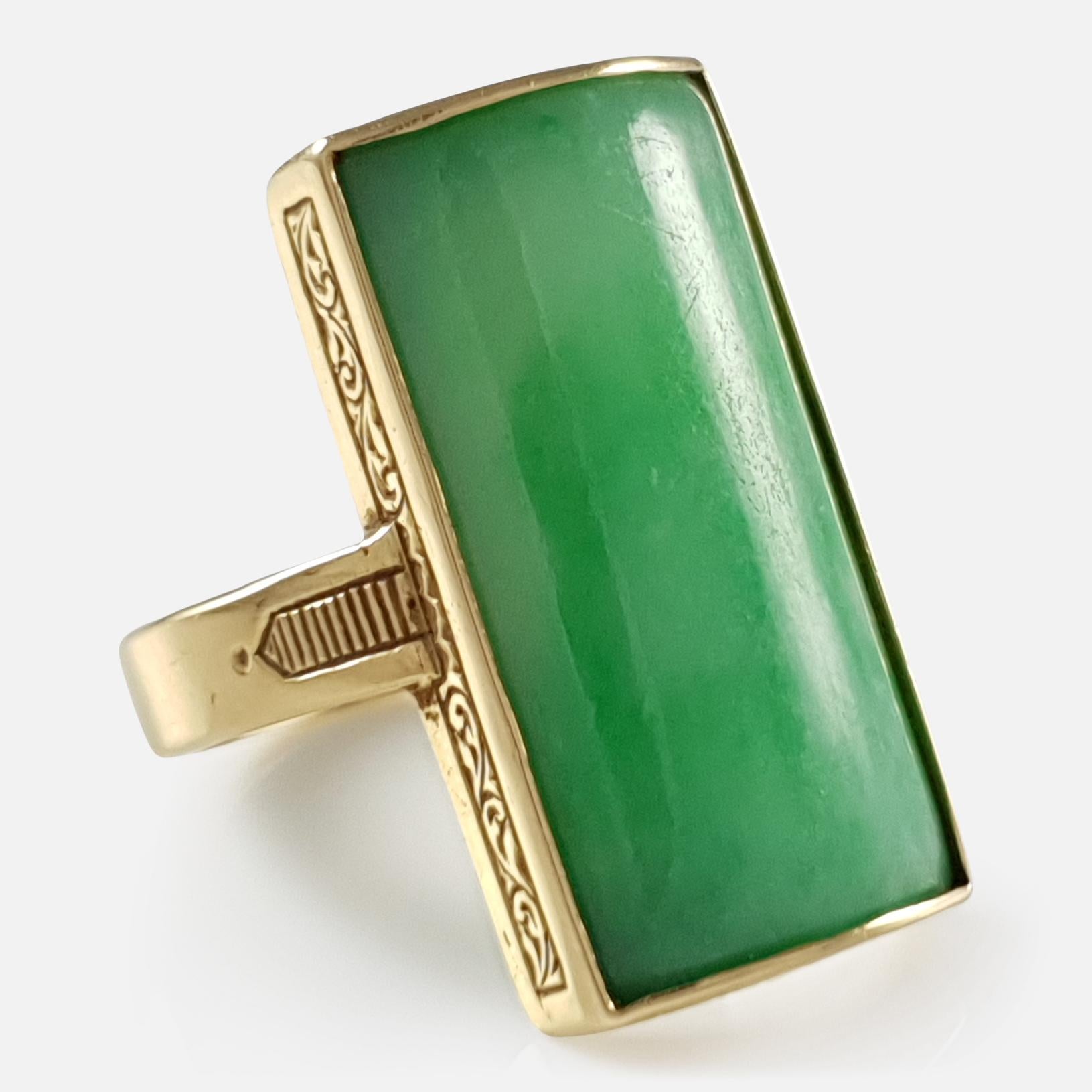 Description: - This is a fine 18 karat yellow gold apple green jade ring - by Bernard Instone 1958. The ring is set with a rectangular curved jade plaque, rub set to a collet with hand engraved scroll and leaf bands, and a flat section shank with