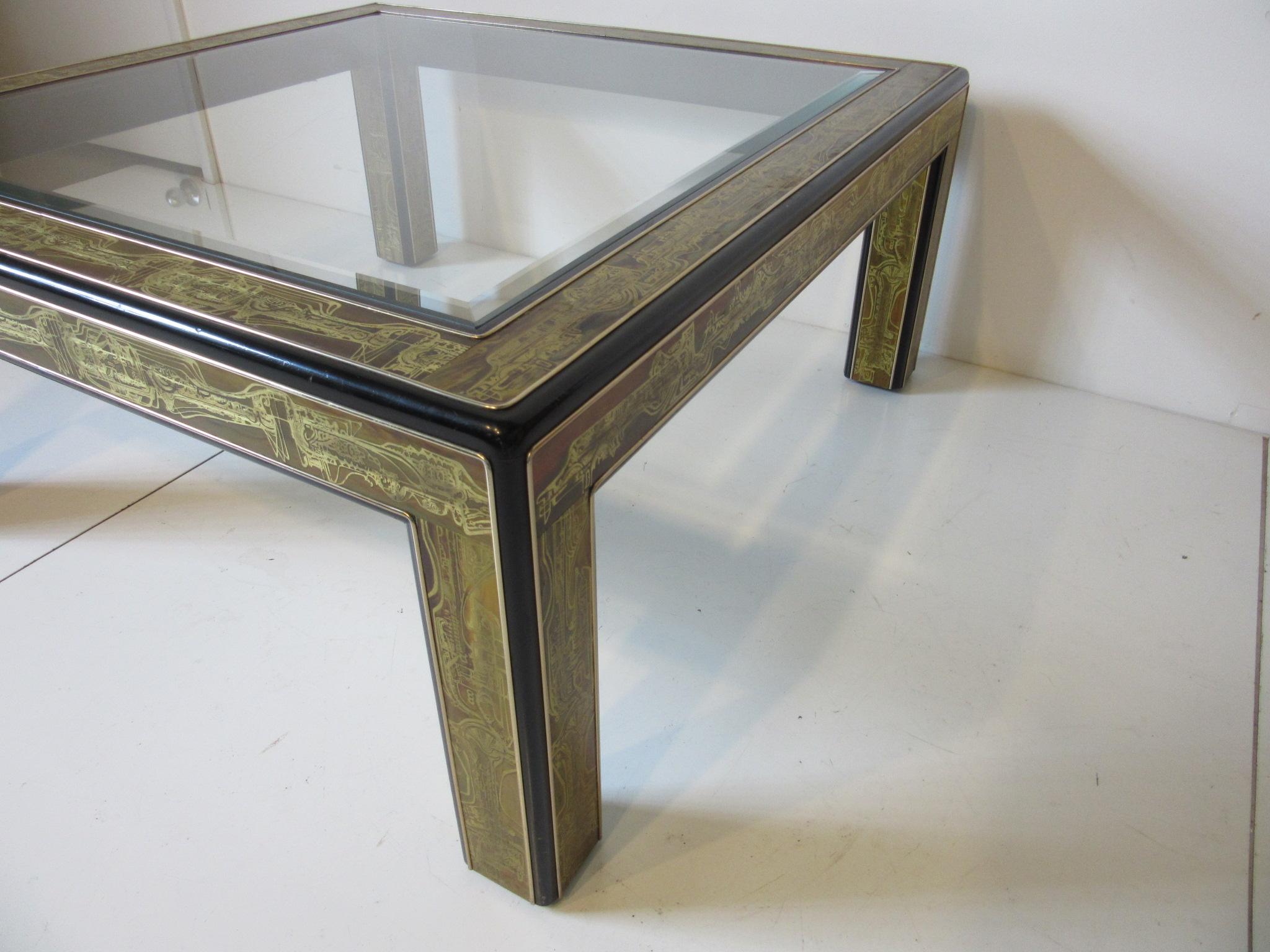 An ebony toned wood framed coffee table with acid etched and patina brass metal detailed inserts with beveled glass top. Manufactured by the Mastercraft Furniture Company Grand Rapids Michigan noted for their high end furnishings.
  