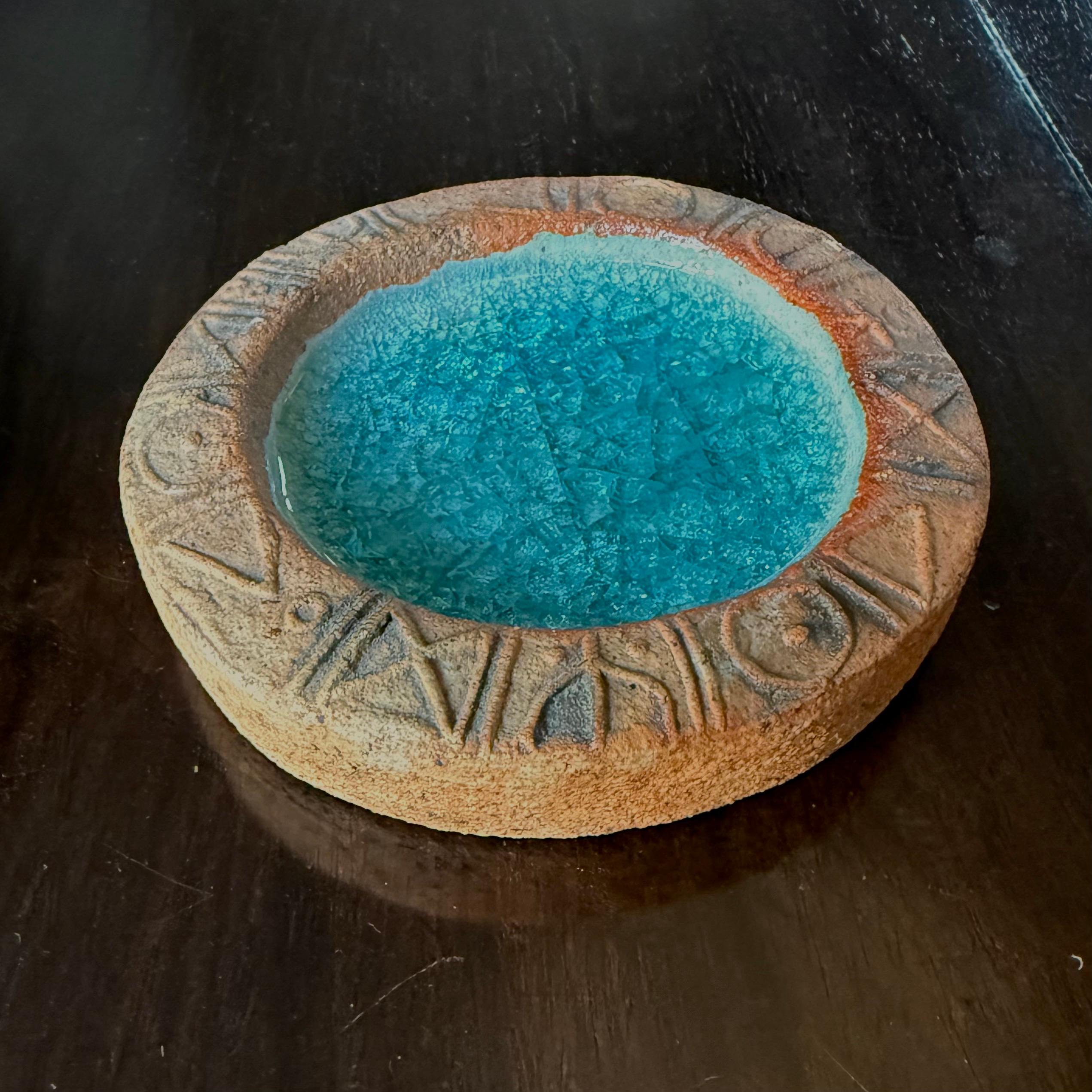 Plato decorativo o vide-poche del ceramista Bernard Rooke. Inglaterra, mediados del siglo XX. Cerámica hecha a mano, en tonos naturales; la base de cristal verde azulado con acabado craquelado. La decoración rúnica propia de Rooke recorre la parte