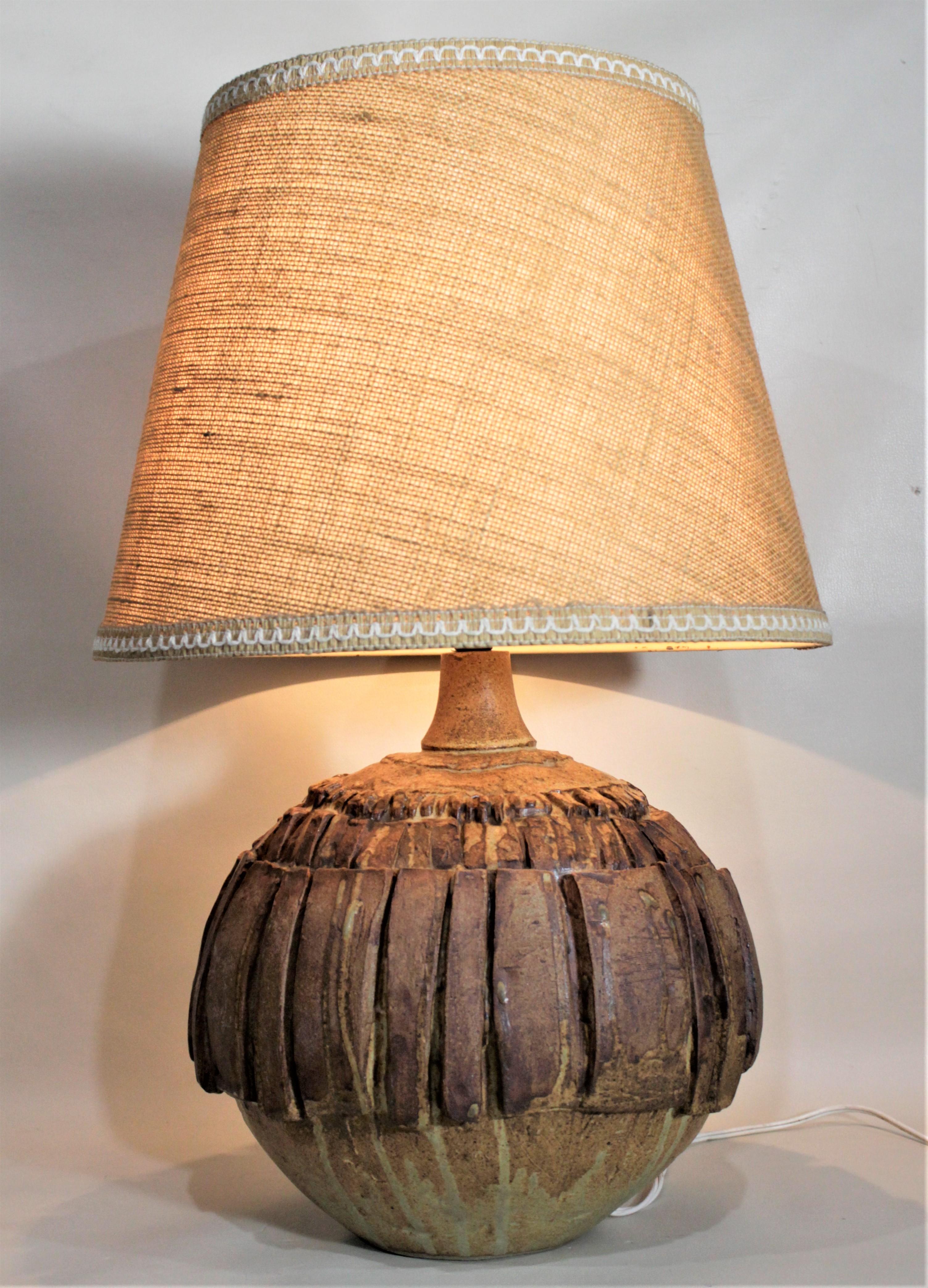 This large and substantial art pottery table lamp was made by Bernard Rooke in England in circa 1965 in the period and style of Mid-Century Modernism. The base of the lamp is done in a brutalistic style using three rows of graduated rough pottery