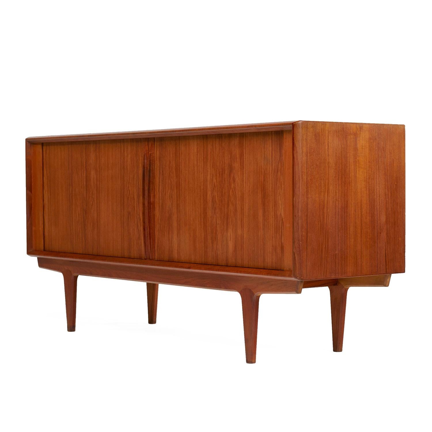 Scandinavian Modern Danish teak tambour door credenza by Bernhard Pedersen & Son. Expertly crafted with sleek lip-like, solid teak carved handles gracing the tambour doors. Open the cabinet to reveal cabinet space at left and right. A stack of three