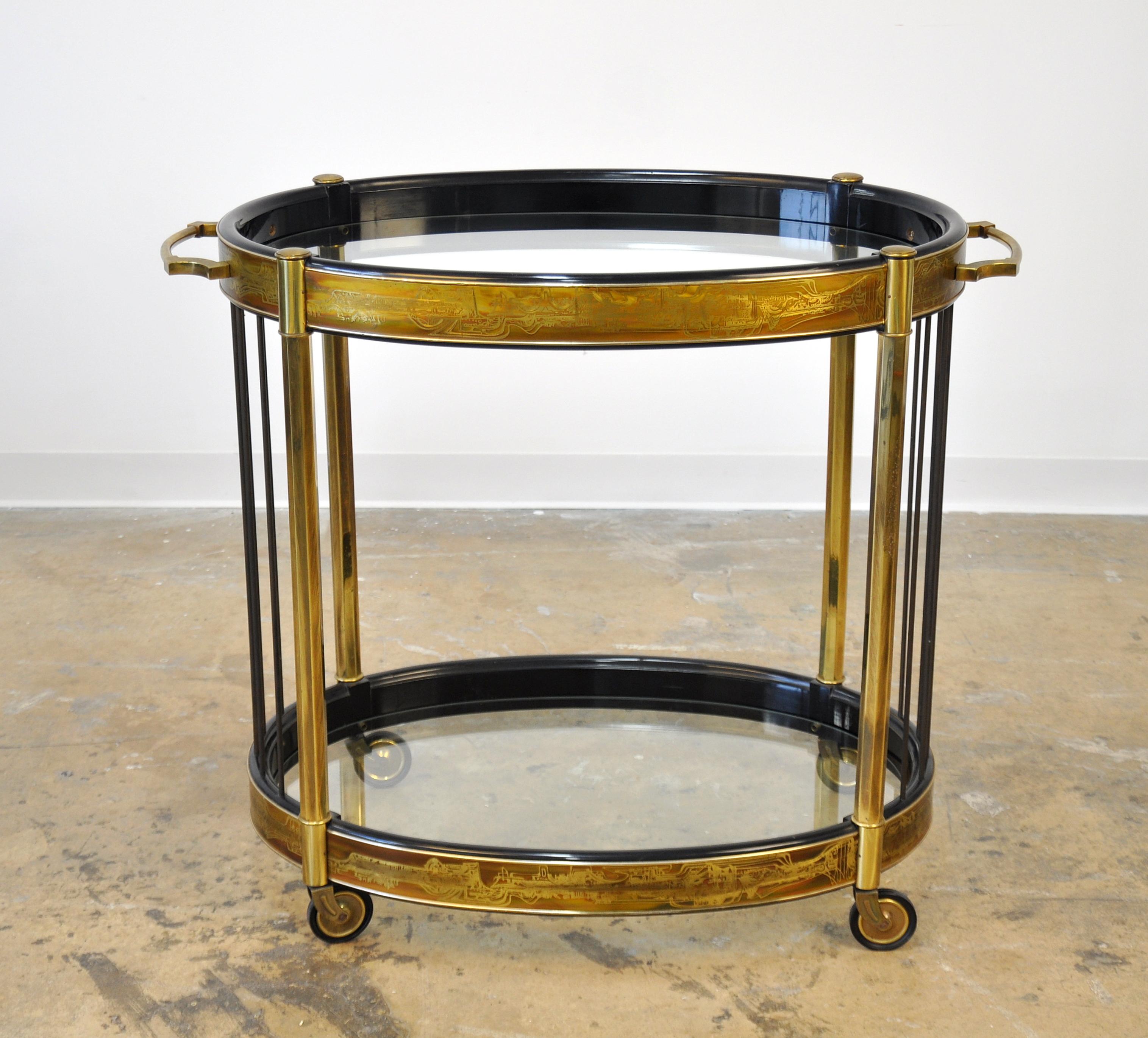 A Hollywood Regency black lacquered wood, acid etched brass and glass rolling, two-tier oval serving trolley, designed by Bernhard Rohne for Mastercraft in the 1970s. The bar or tea cart features: solid brass legs and handles; patinated brass rods;