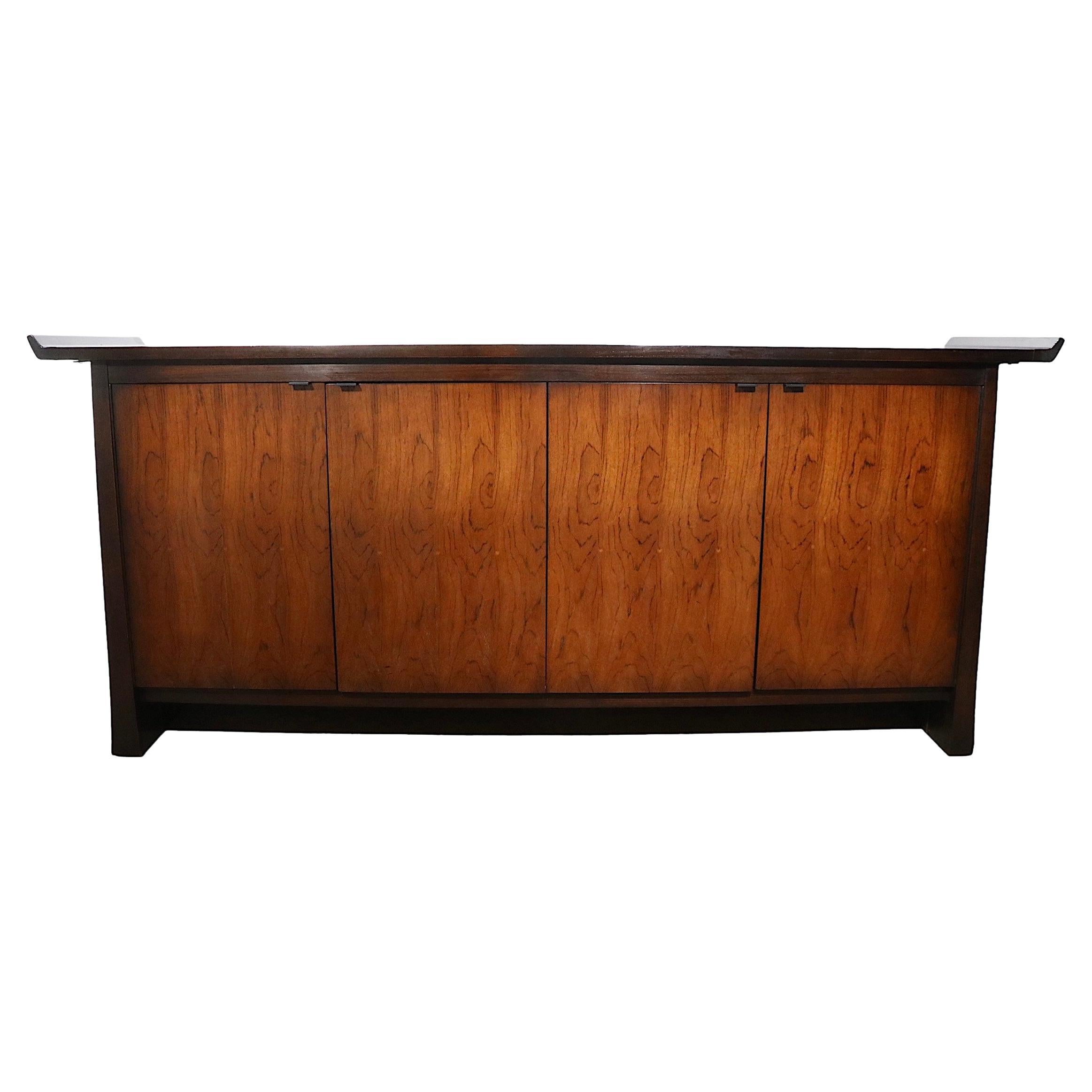 Elegant and sophisticated Asia Modern style credenza made by Bernhardt as part of their celebrated Flair line. This chic sideboard features a dark stained oak case with vibrant book matched rosewood veneer doors (4) which open to reveal open shelved