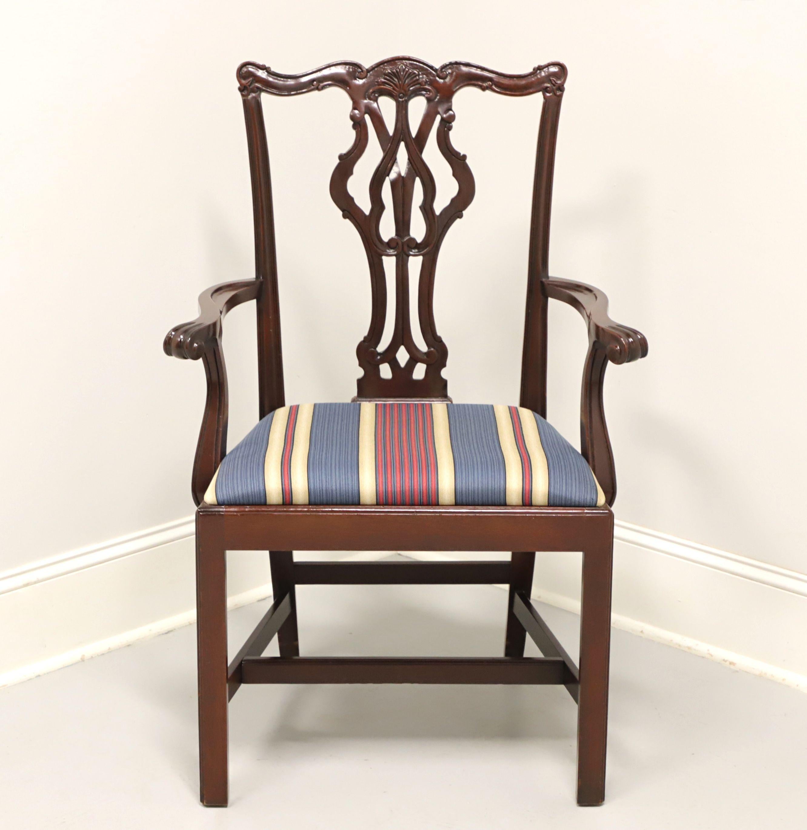 A Chippendale style armchair by Bernhardt. Solid mahogany with elaborately carved crest rail & backrest, curved arms with arched supports, straight legs, and stretcher base. Blue, pink and beige stripe pattern fabric upholstered seat. Made in the