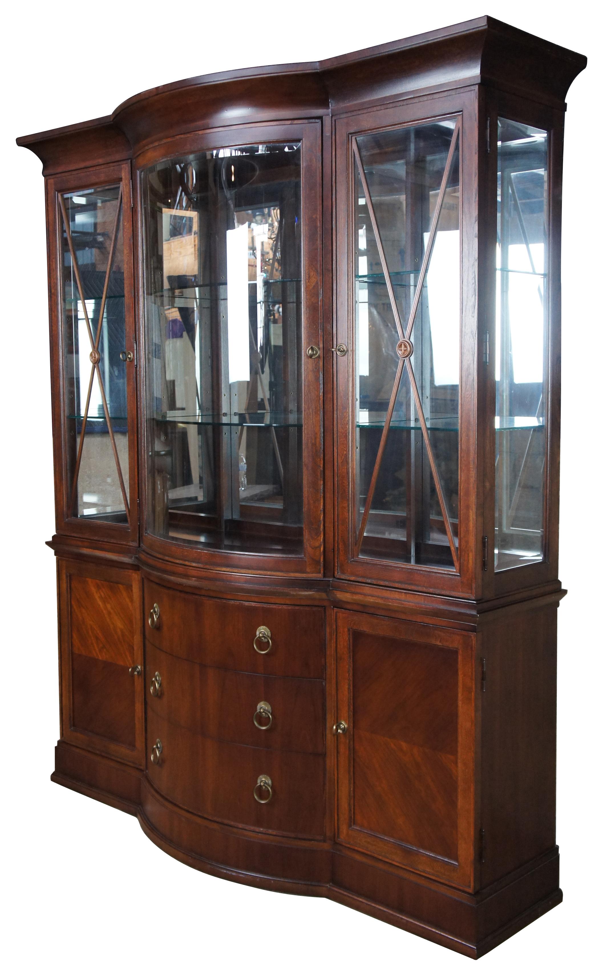 Vintage Bernhardt walnut china cabinet, measures: 86”. Features a bow front with neoclassical styling, adjustable glass shelving, three drawers (one lined with felt), and two cabinet doors. Illuminates to display your curiosities or china figurines
