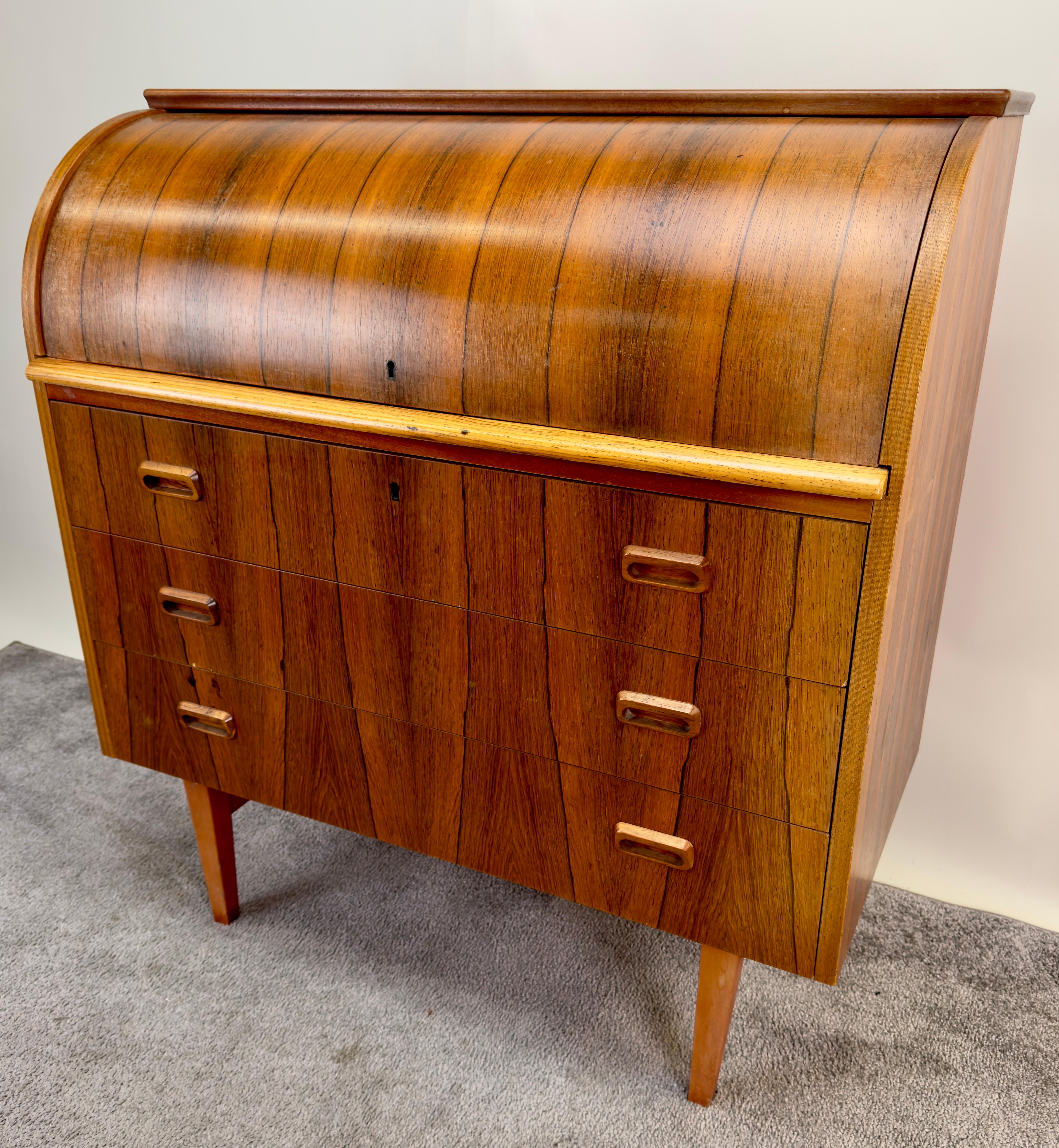 A rare Bernhardt Pedersen & Son Danish Mid Century Modern roll top writing desk crafted from beautifully grained rosewood, the desk emanates a warm and inviting aura, drawing attention to the inherent beauty of the wood. One of the standout features