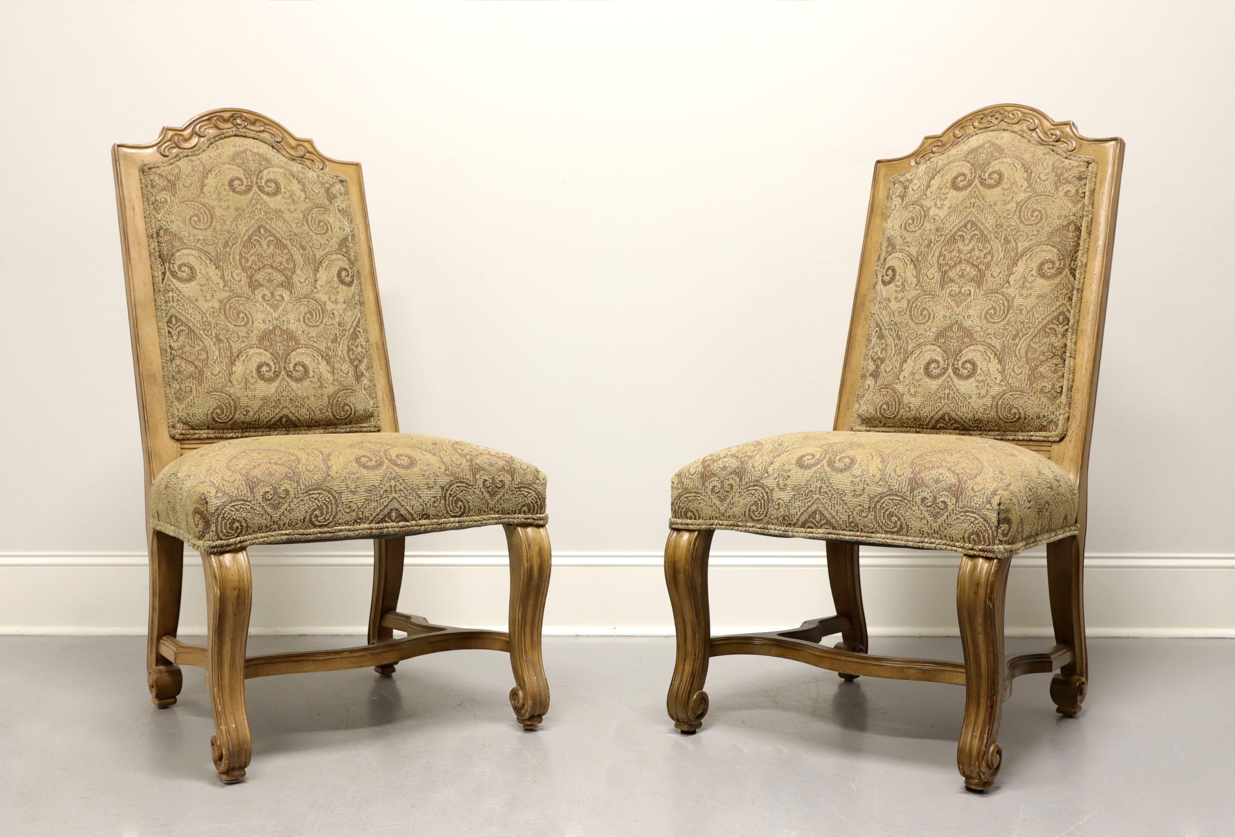 A pair of Rustic Italian style dining side chairs by Bernhardt Furniture. Solid wood frames with a distressed finish. Arched top to seat backs, carved curved legs and stretcher base. The high seat backs are upholstered with a tapestry like raised