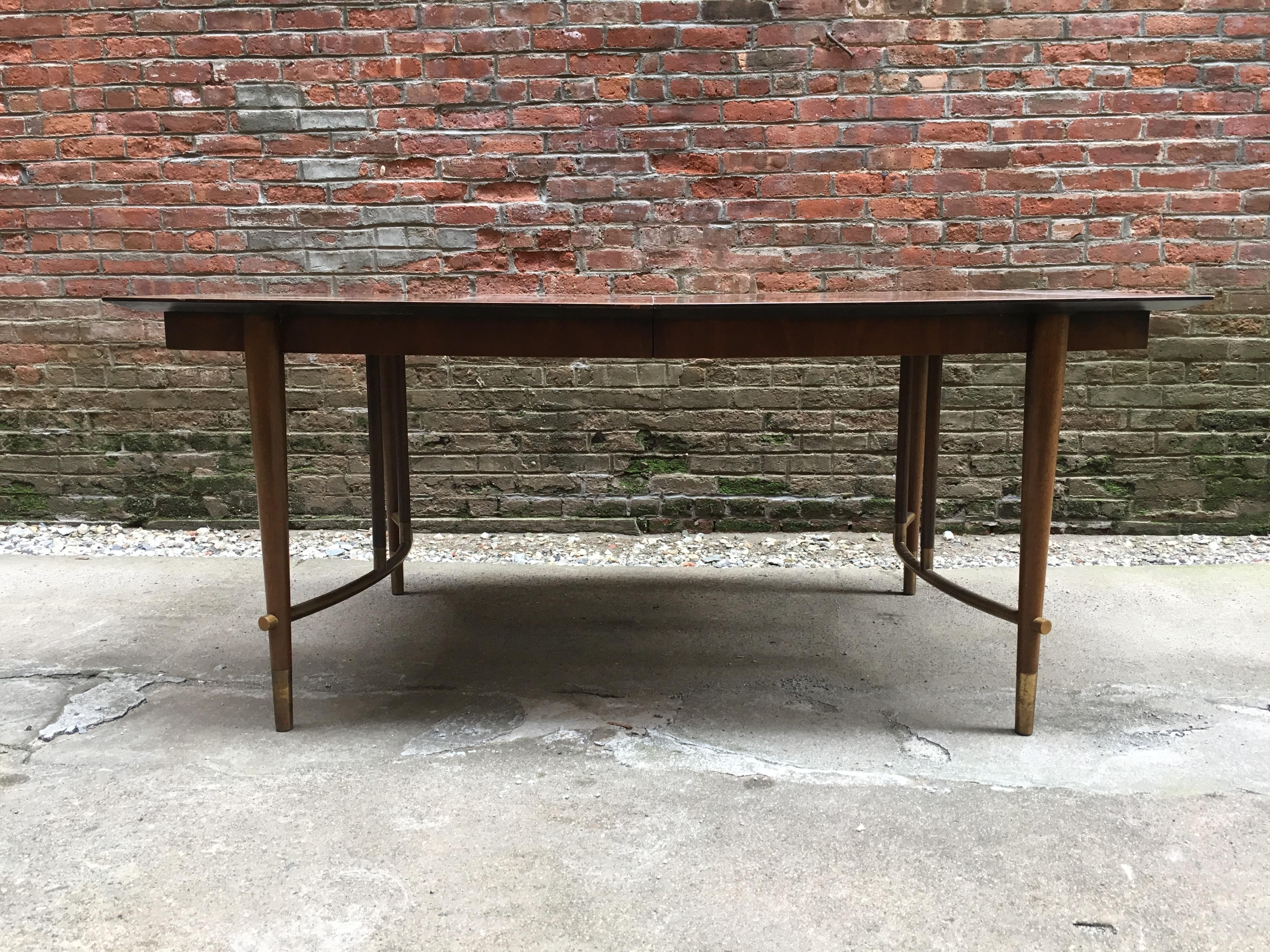 Stylish dining table designed by Bert England for Johnson Furniture Company, grand rapids, Michigan, circa 1960. Beautiful figured walnut veneers with brass base accents and sabots. Three extension leaves for more space and guests. Very good