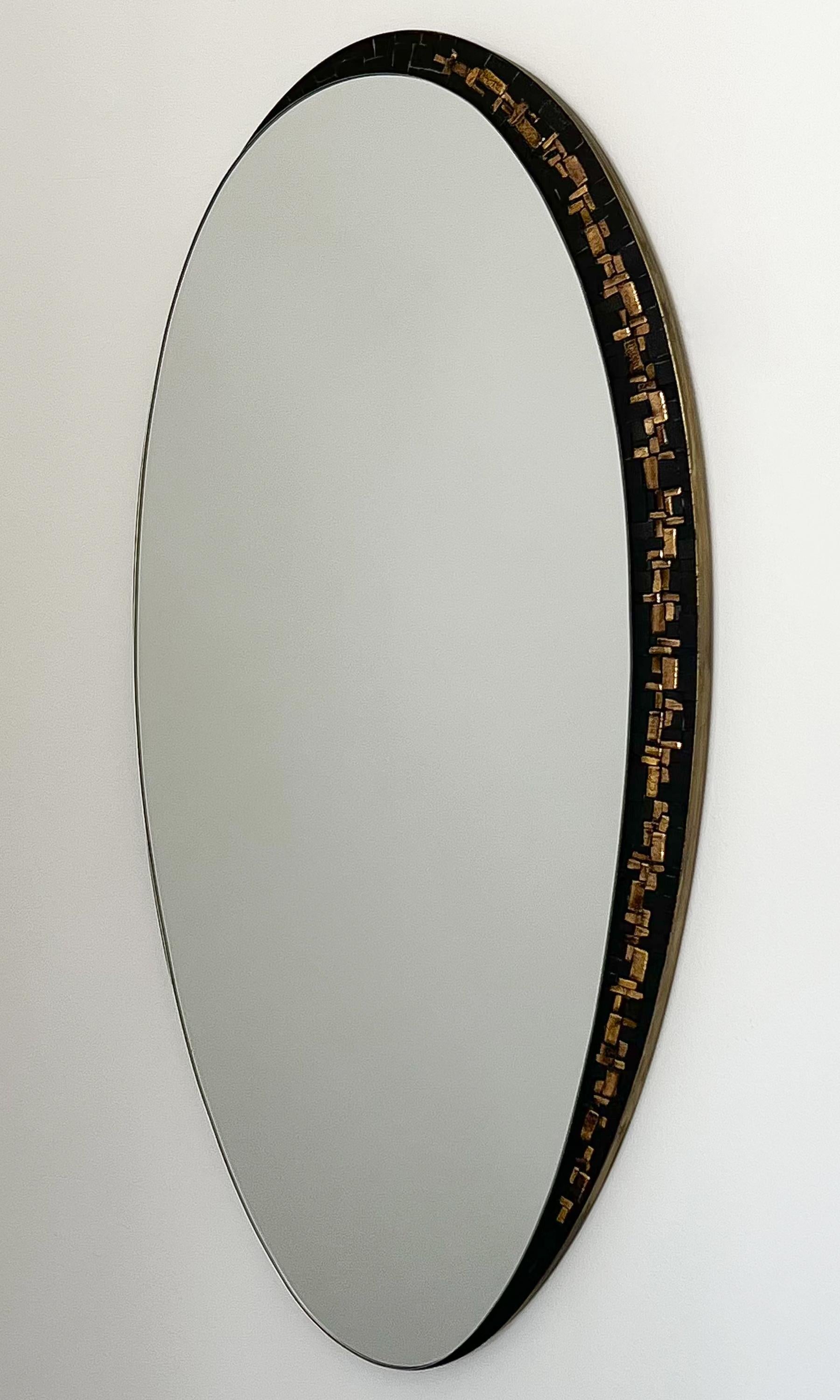 Berthold Müller-Oerlinghausen black and gold mosaic tiled oval wall mirror, Germany circa 1950s. Oval mirror with a crescent of matte black and gold metallic mosaic tiles on the right side. Asymmetric and modern in design. Entire mirror is framed in