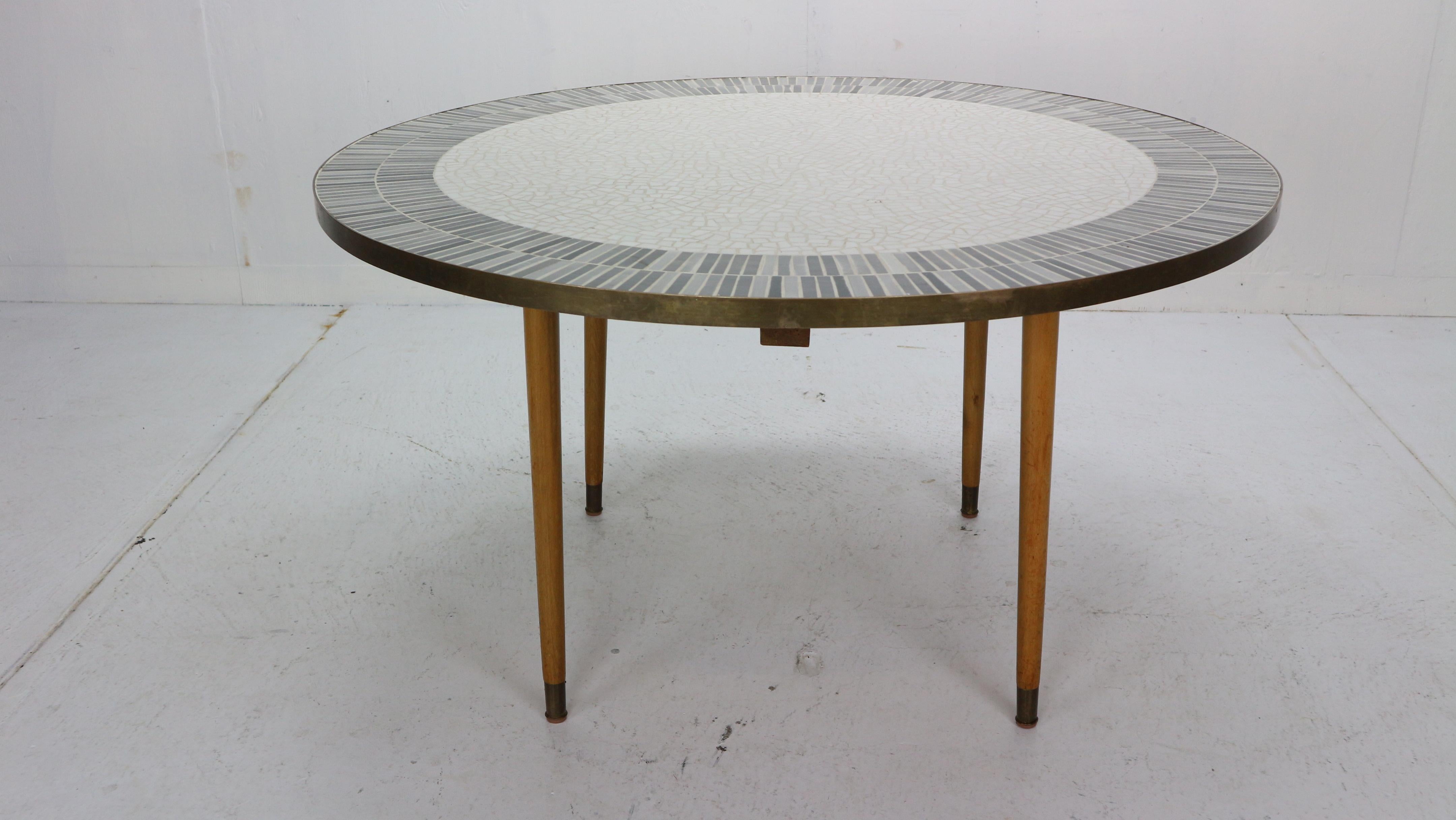 Round Mosaic top coffee table with a brass band around it on four brass and teak legs, by Berthold Muller, 1960s period, Germany.
The top has a beautiful abstract mosaic composition. Great elegance and rarely encountered. Muller-Oerlinghausen