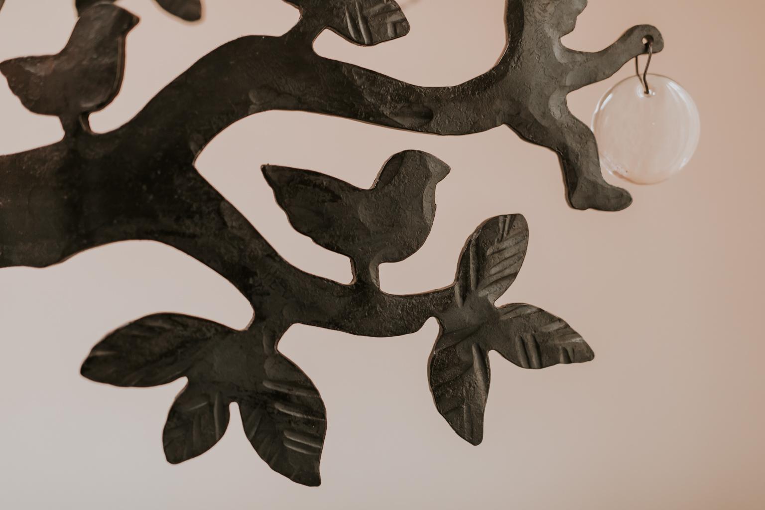 This is a whimsical iron forged tree. Designed by Bertil Vallien and produced by Boda Smide. 
In among the branches are silhouettes of leaves, birds and figures, glass drops and seven tea light holders. 
Measures: 68 cm high x 70 cm long and 28 cm