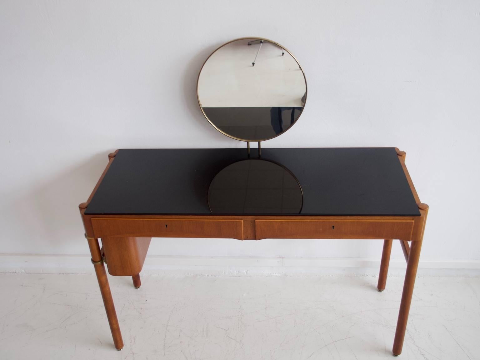 Teak vanity with a round mirror and dark mirrored glass tabletop. Designed by Bertil Fridhagen and manufactured by Bodafors, Sweden, in 1957. Two drawers with beech interior and a movable compartment for smaller items underneath. Key included.
