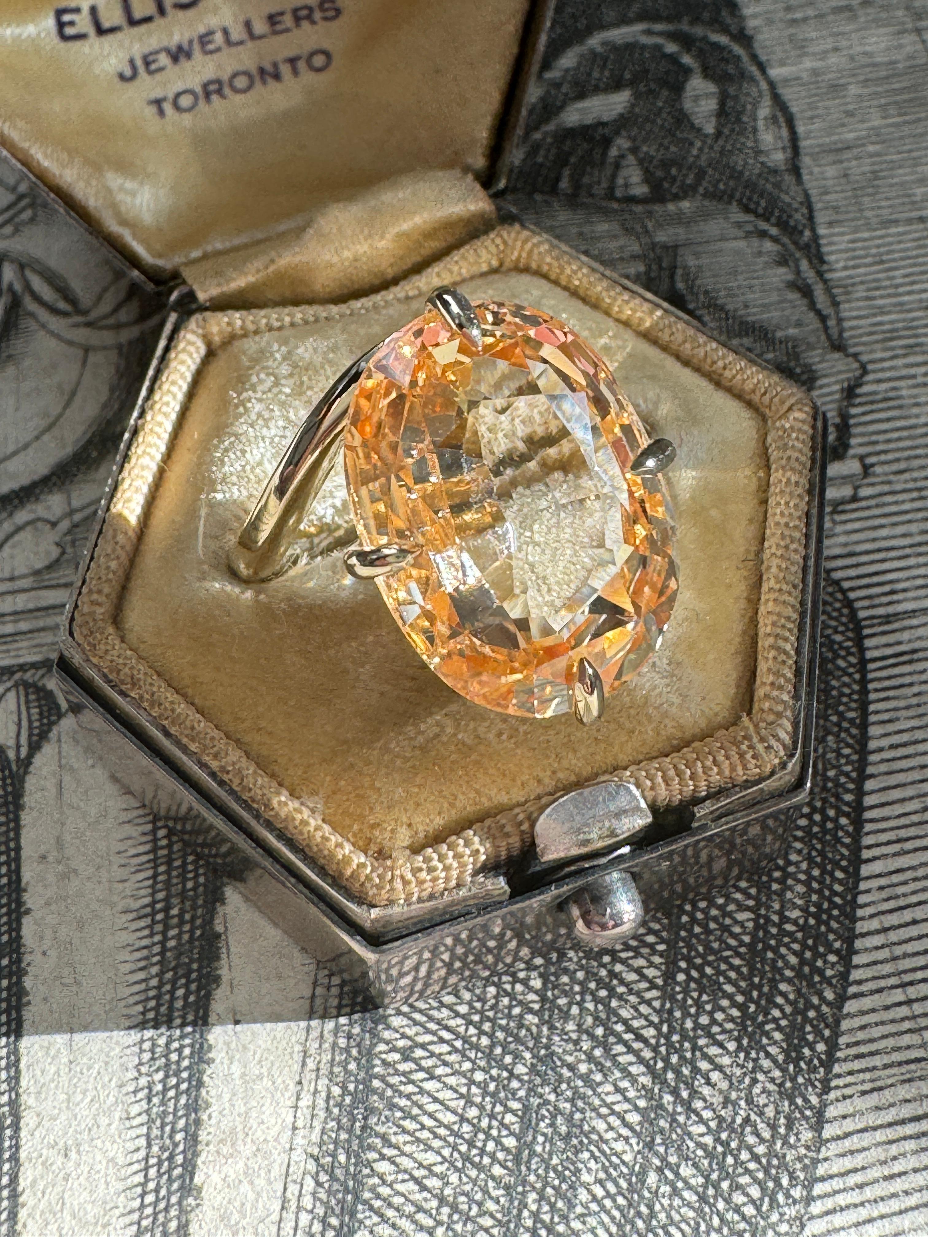 Ein heller und fröhlicher goldener Saphir von 13,81 Karat strahlt aus einer schlank gestalteten 14-karätigen Goldfassung mit handgeschliffenen Adlerkrallen an den Himmelsrichtungen. Der Saphir ist ein antiker Stein aus der Zeit des Art déco. Derzeit