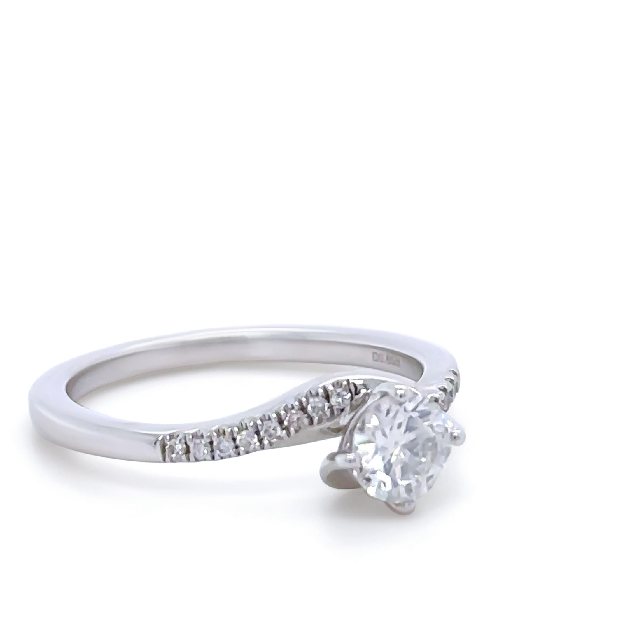 Un anillo de compromiso de diamantes a medida, de oro blanco de 14 ct. Con un diamante talla brillante redondo en un engaste de cuatro garras, que mide 5,04 - 5,07 mm de diámetro y pesa 0,49 ct.

Además, está engastada con 16 diamantes redondos