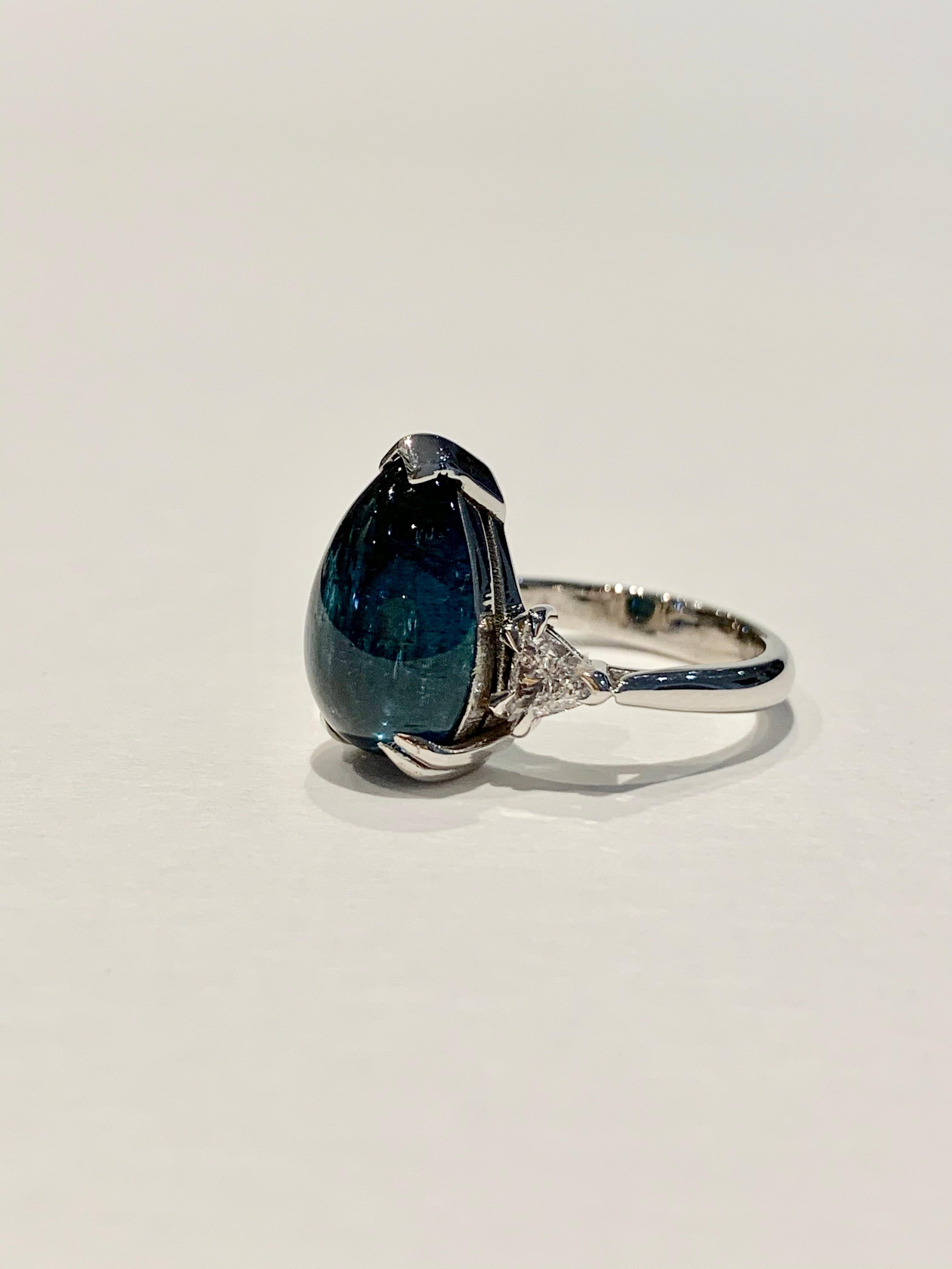 This amazing blue Tourmaline* pear cut cabochon* is eye clean and set in a double claw design in 18ct White Gold.  A BESPOKE design using a CAD  to ensure this stone was presented as its best.  The ring also has 2 x .20 Trillion Cut diamonds as