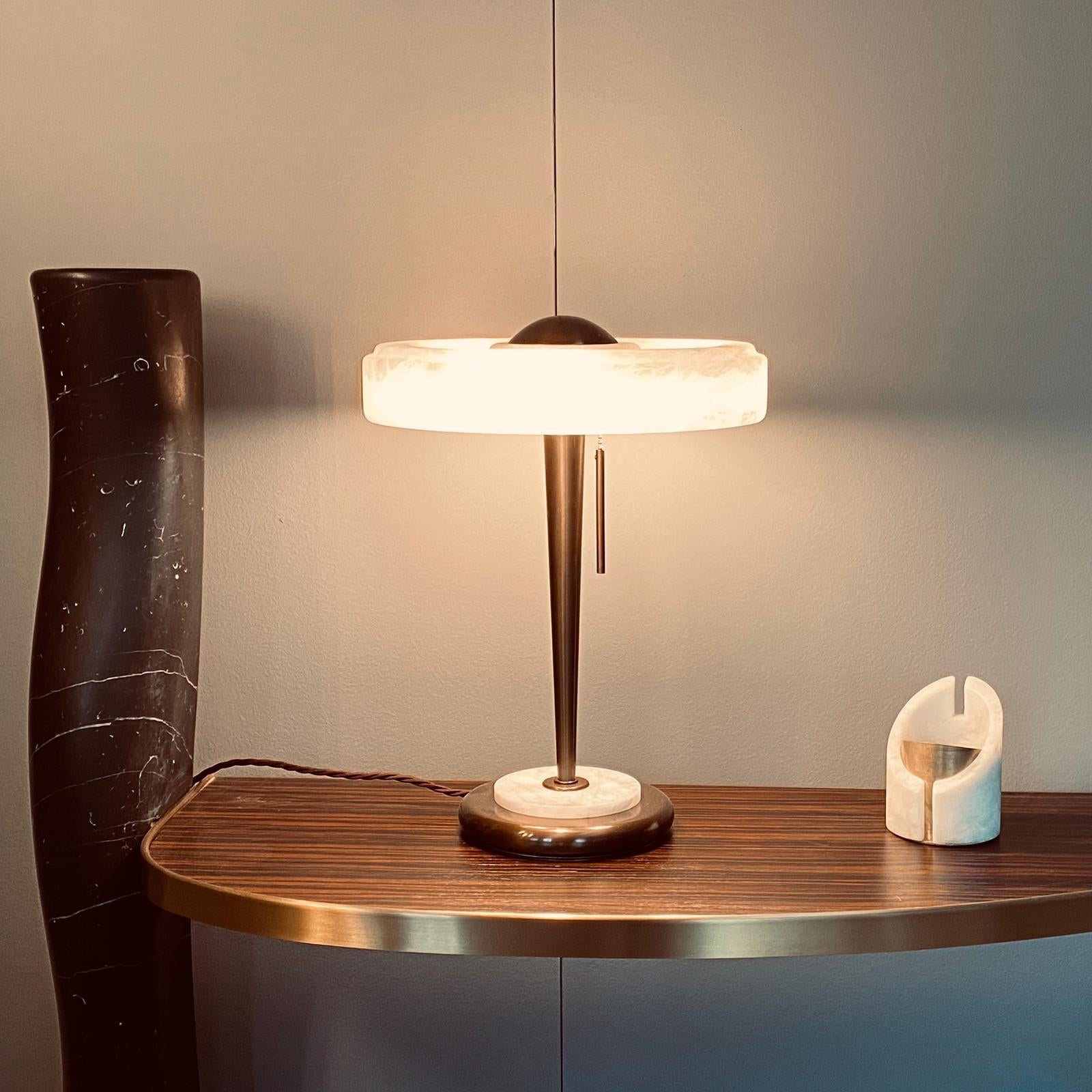 Cosulich Interiors in collaboration with Matlight: An Art Deco style organic table or desk lamp with a retro aesthetic, handcrafted in limited series of 10 pieces in Italy.
The aerodynamic flat design shade, raised on an elegant bronze finish