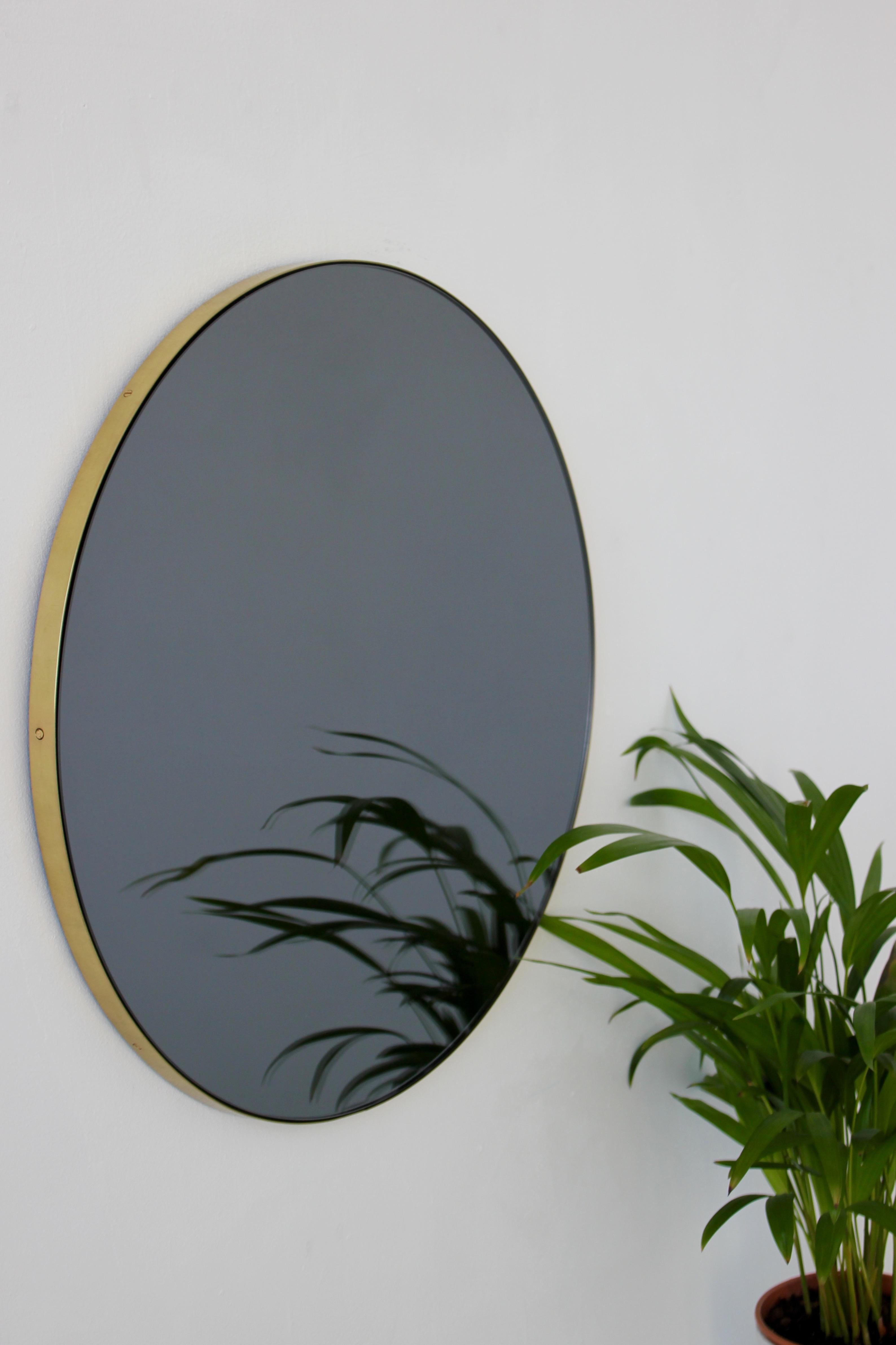 Miroir rond Orbis™ minimaliste teinté de noir avec un élégant cadre en laiton brossé. Les détails et la finition, notamment les vis apparentes en laiton, soulignent le caractère artisanal et la qualité du miroir, véritable signature de notre marque.