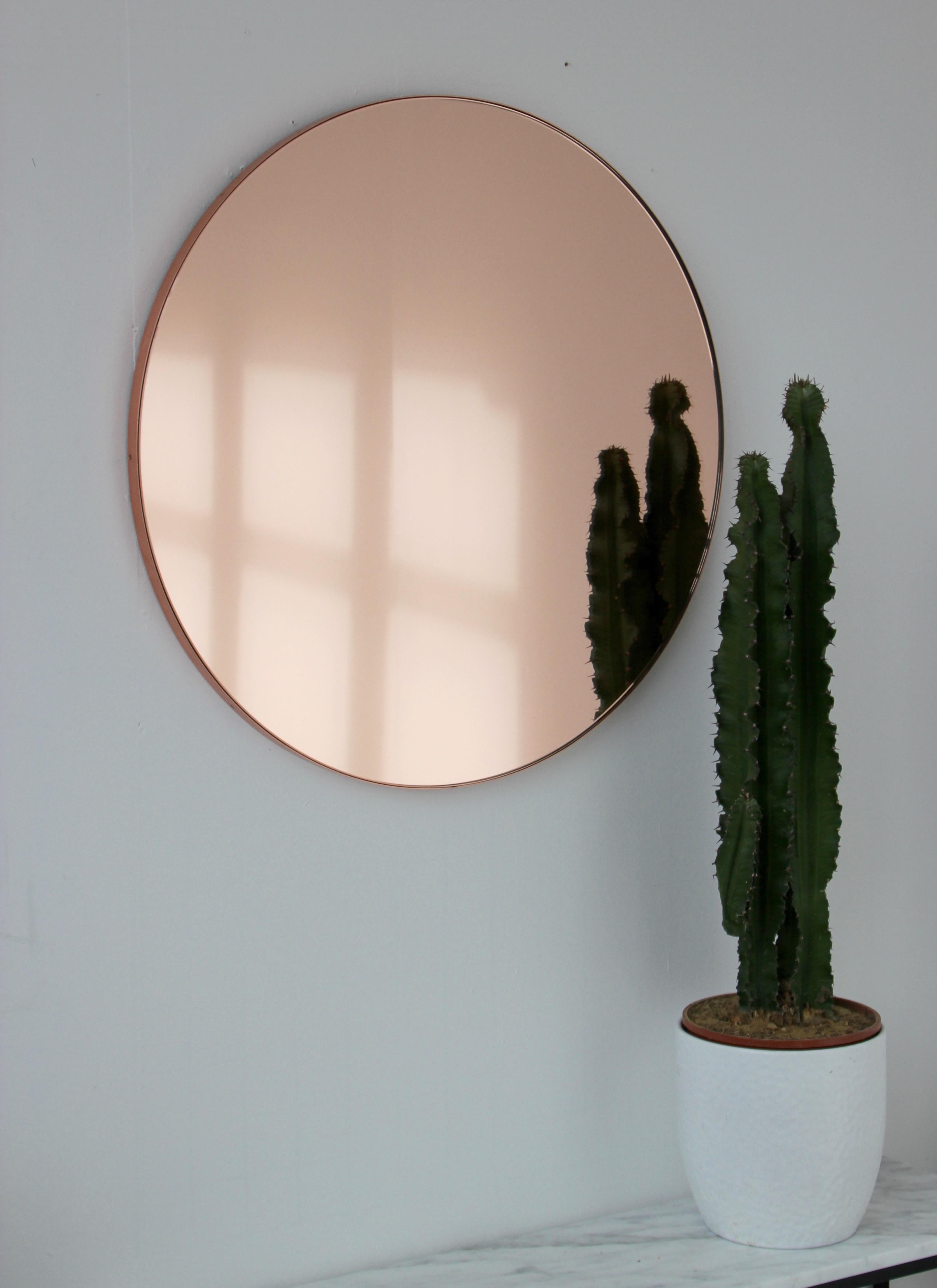 Contemporary rose gold / peach tinted round mirror with an elegant brushed copper frame. The detailing and finish, including visible copper plated screws, emphasize the crafty and quality feel of the mirror, a true signature of our brand. Designed