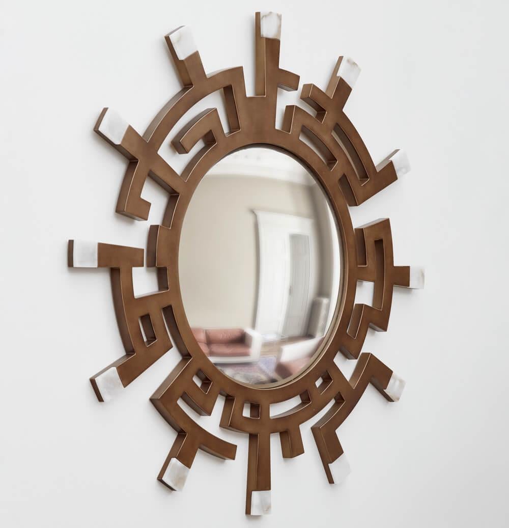 The “Circe” model is a visually striking convex mirror, featuring a bronze frame with elegant geometric patterns. The alabaster tiles, precisely set at the ends of the frame, offer a refined contrast between the warmth of the bronze and the natural