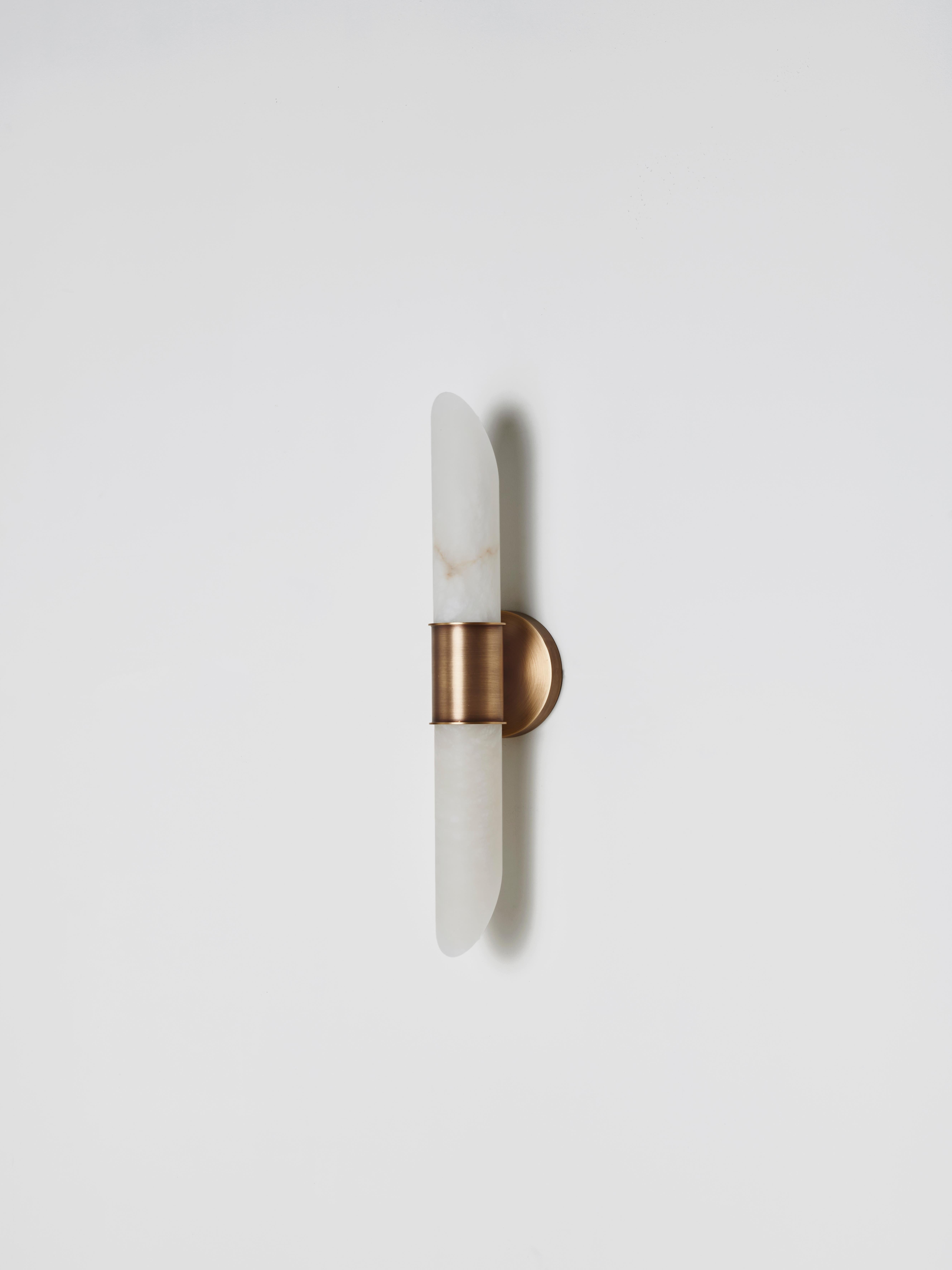 The Tabitha wall lamp combines the timeless elegance of alabaster with the modernity of brushed brass. The alabaster tubes, cut with a diagonal “salami slice” style, give the lamp a distinctive character, creating a play of light and shadows that
