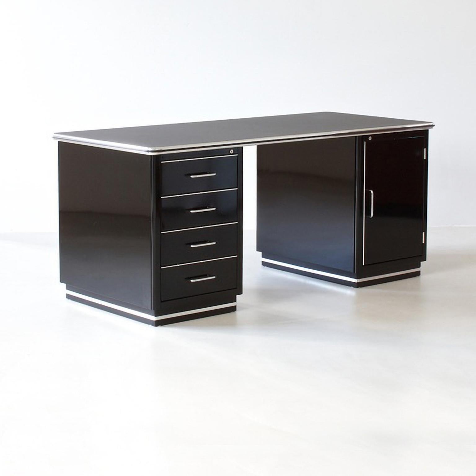 Scrivania direzionale in metallo dal classico design industriale. La forma semplice e senza tempo con due cassetti crea uno spazio di lavoro pulito e di grande impatto che si adatta a diverse situazioni di interior design. Il piano del tavolo può
