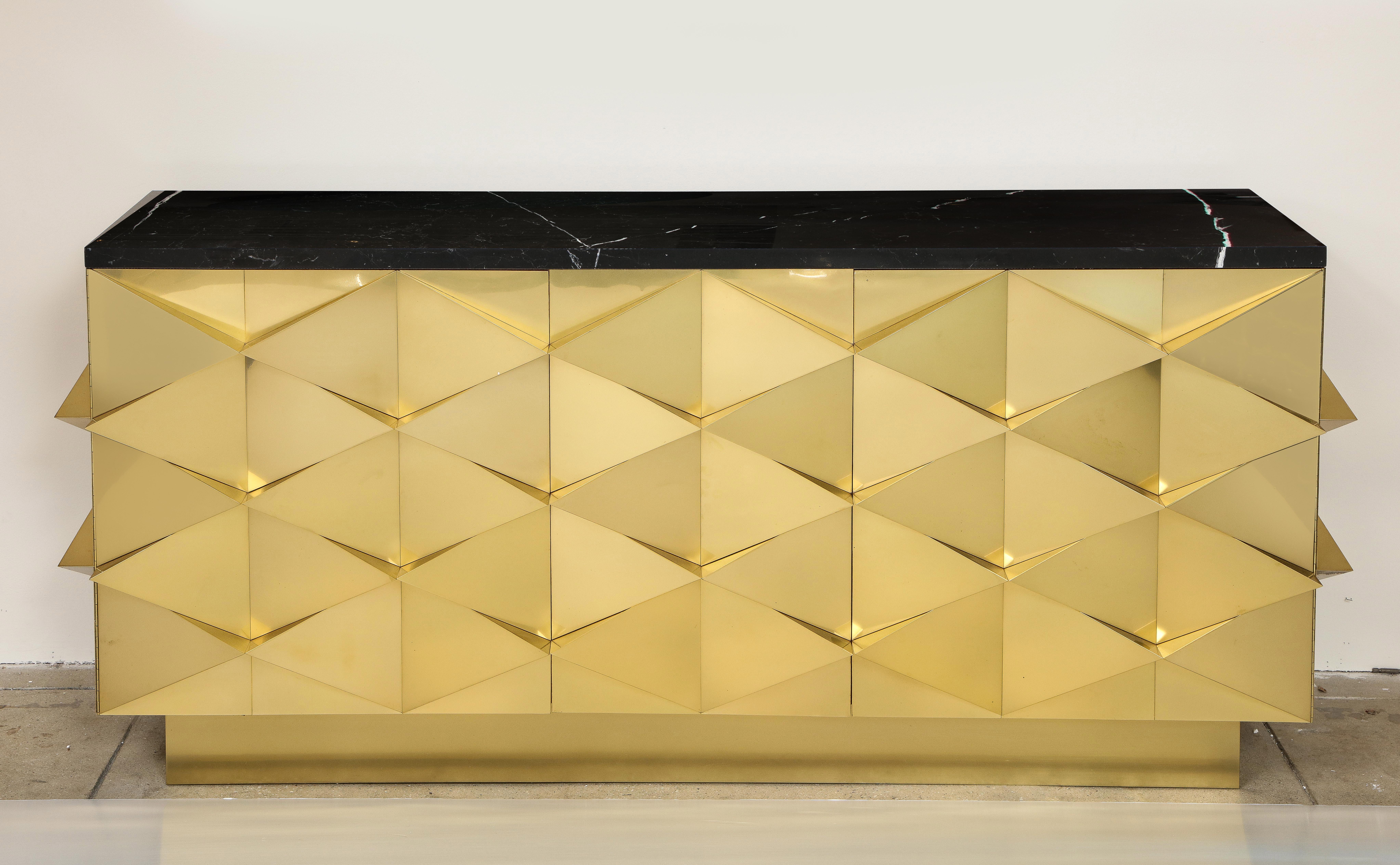 Bespoke lacquered brass and black Marquina marble top sideboard or credenza completely hand-crafted by a master artisan in Italy, 2022. Handcrafted wooden cabinet with projecting geometric shapes is clad or veneered in lacquered brass, creating a