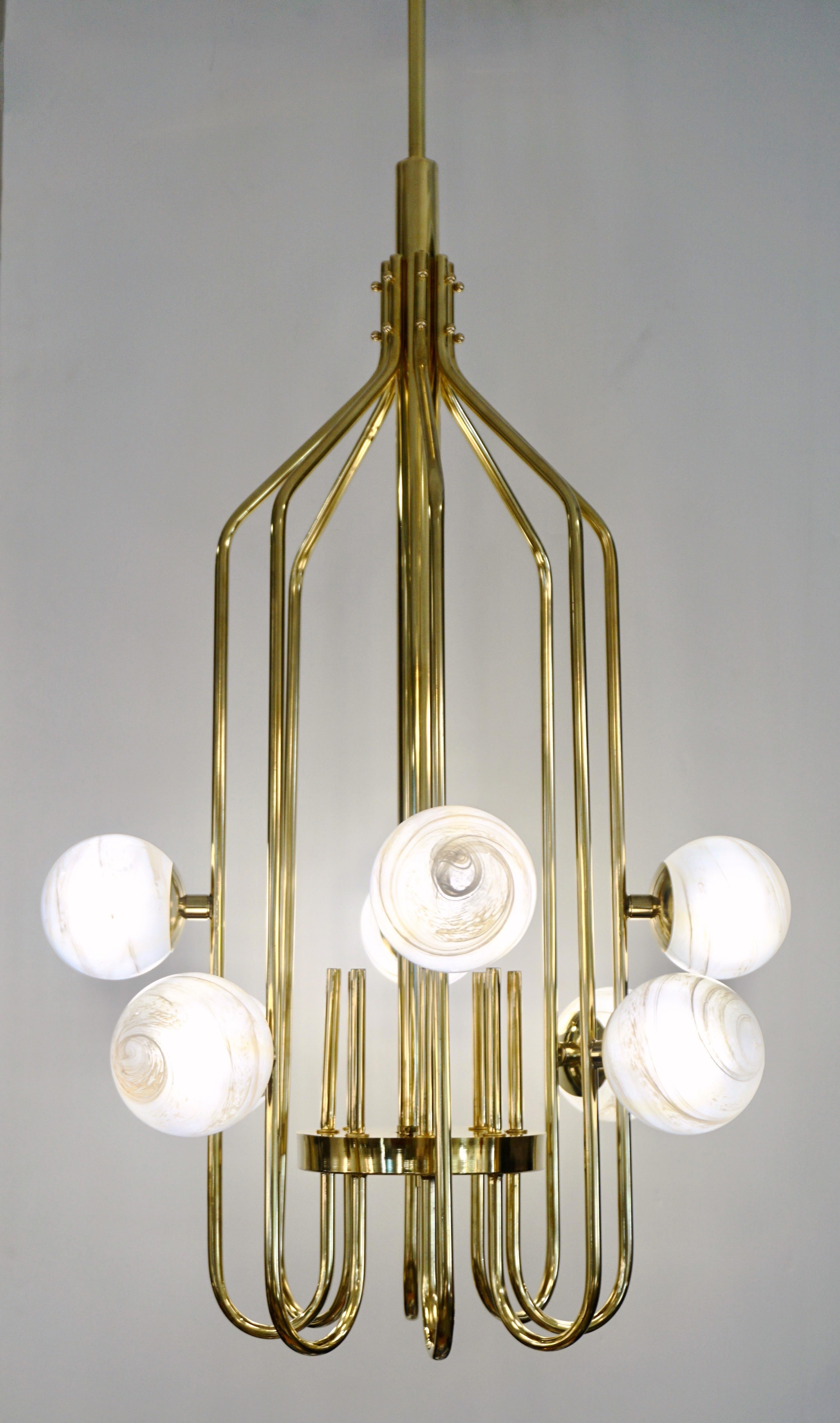 A contemporary innovative custom modern chandelier, entirely handcrafted in Italy. The handmade geometric cylinder brass structure, resembling a sleek birdcage, has a very organic curvilinear shape decorated with 8 round globes in an innovative