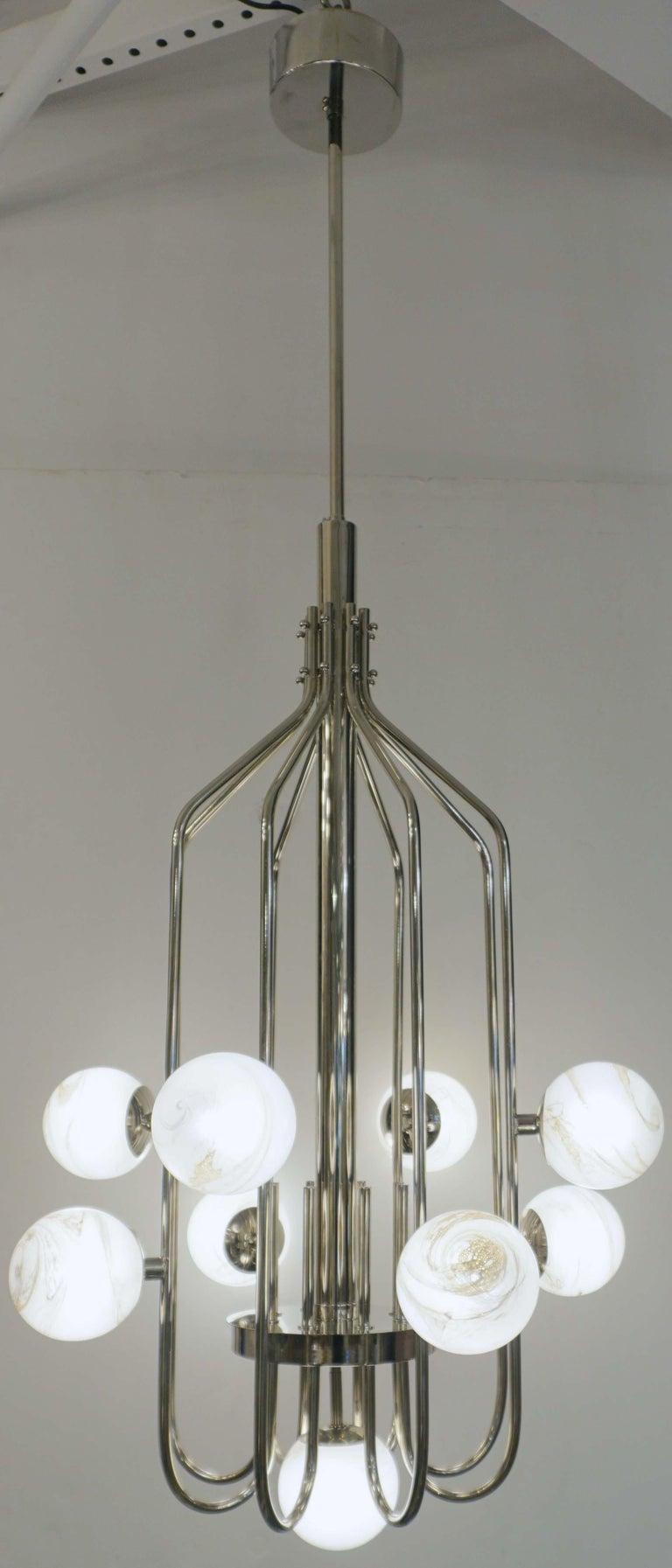 A contemporary innovative custom modern chandelier, entirely handcrafted in Italy. The handmade geometric cylinder nickel structure, resembling a sleek birdcage, has a very organic curvilinear shape decorated with 9 round globes in an innovative