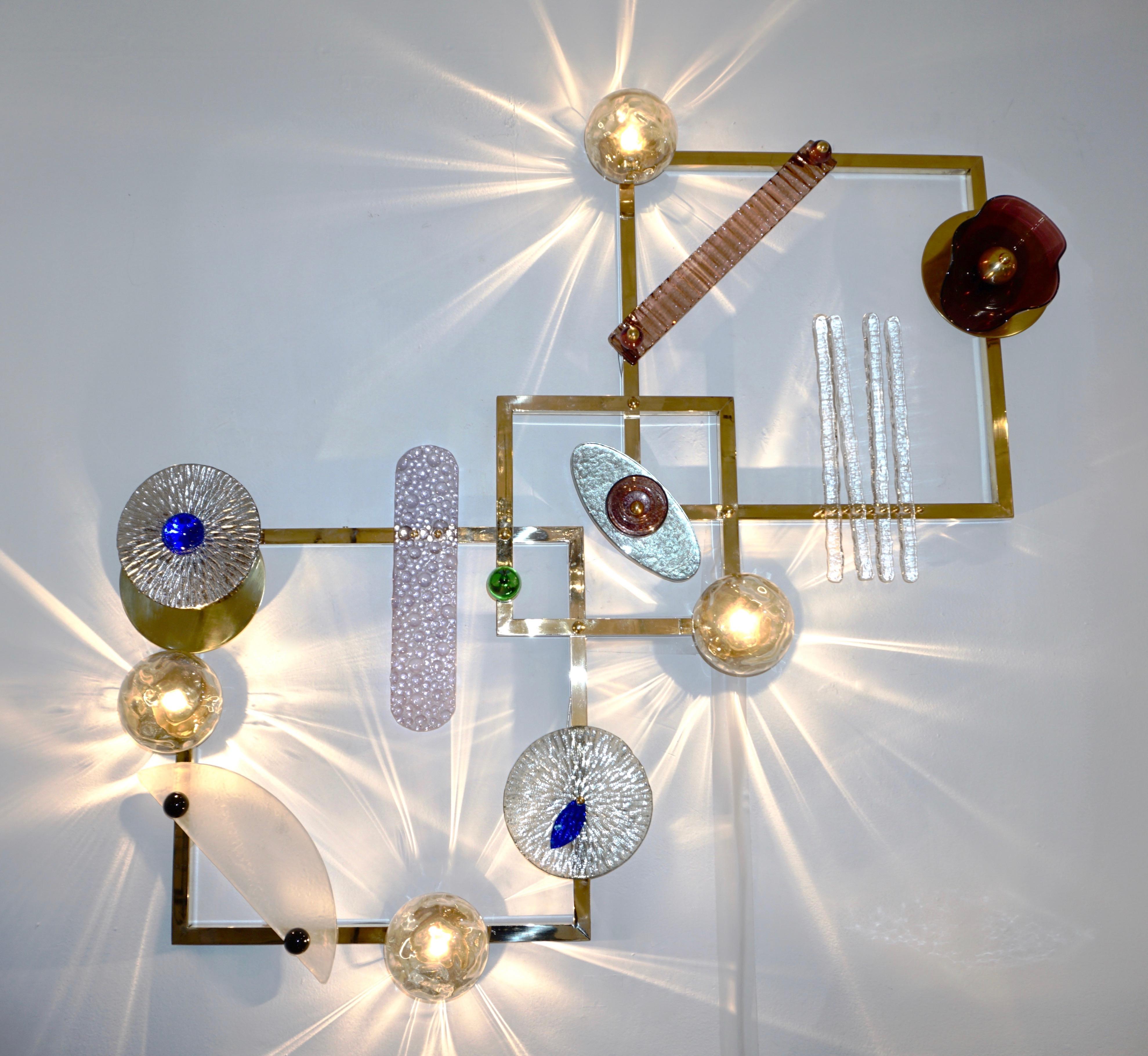 An exclusive illuminating Work of Art, wall light and art sculpture, entirely handcrafted in Italy, of geometric organic design, consisting of 2 square brass frames diagonally linked by a smaller one, decorated by hand made brass and Murano glass